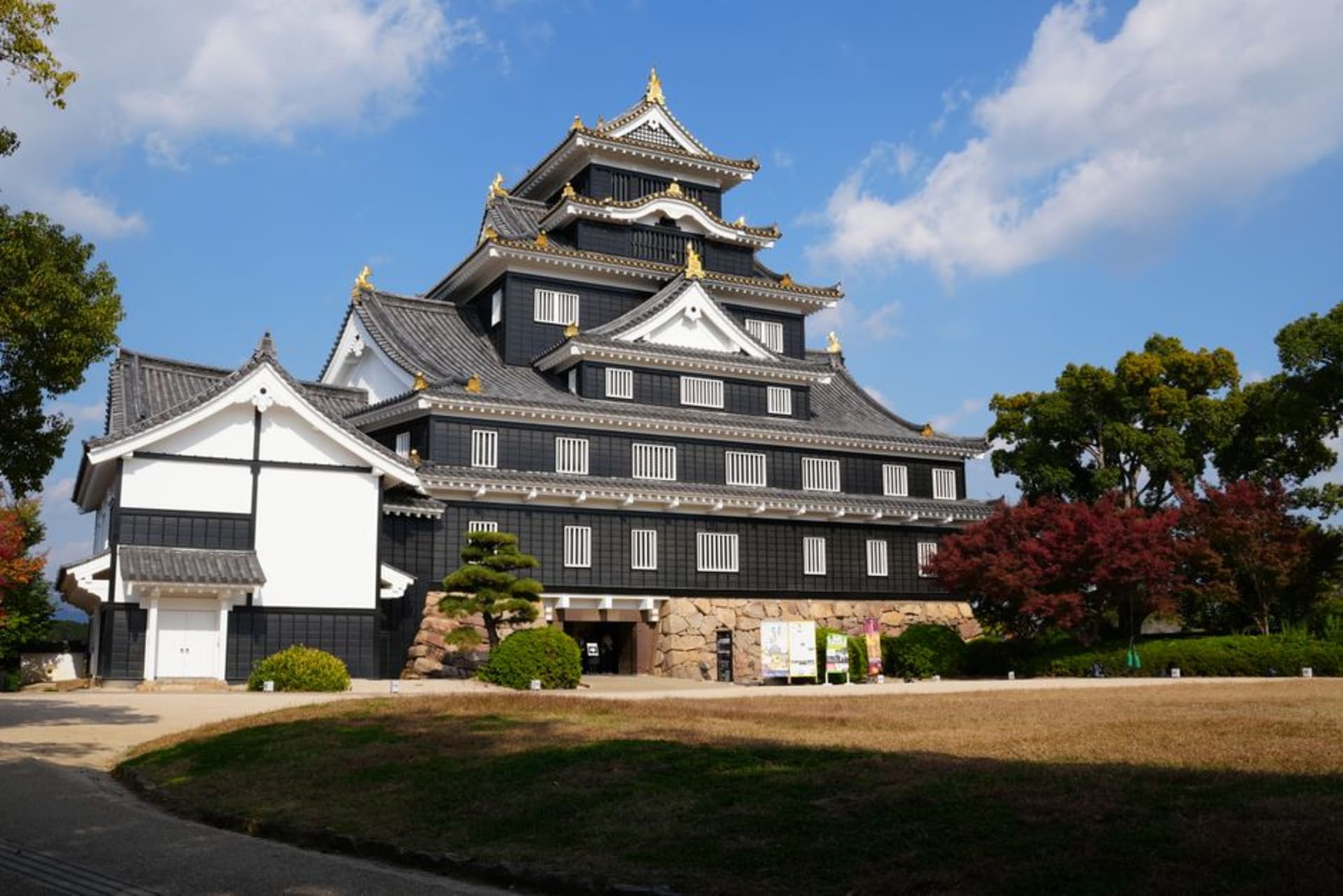 The white keep of Wakayama Castle rising above green trees and stone walls in the city