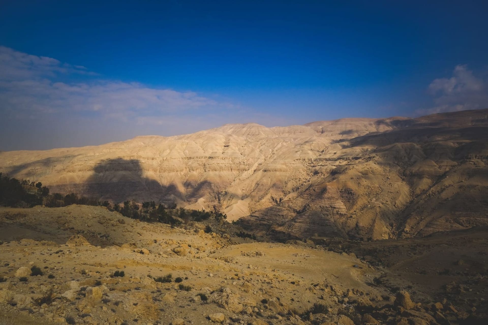 A narrow sandstone canyon with turquoise water rushing through its base, sheer rust-red cliffs rising on both sides, a hiker chest-deep in the current reaching for a rope near a small waterfall.