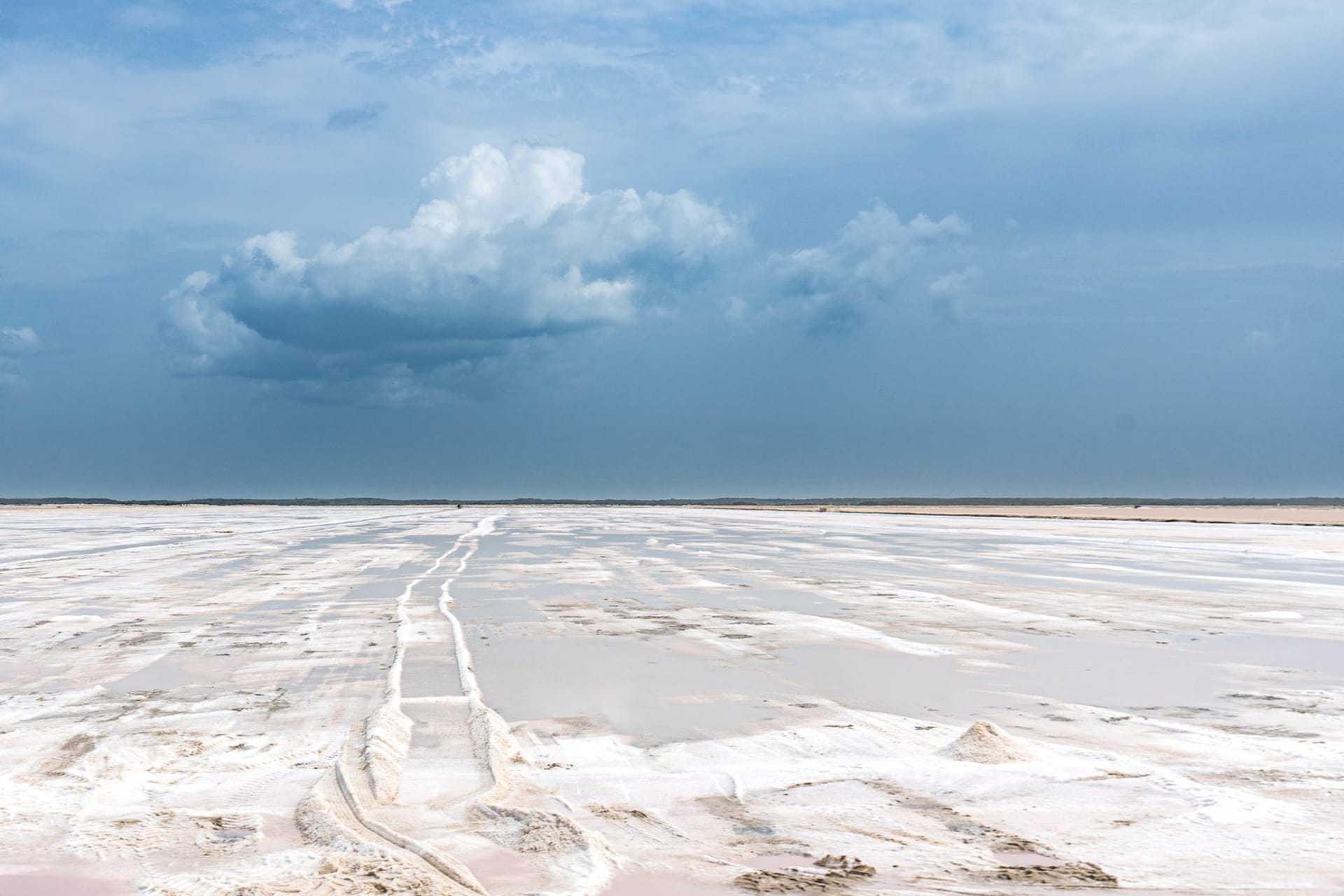 An infinite expanse of cracked white salt at the Makgadikgadi Pans, a lone meerkat standing upright on a termite mound against an enormous blue sky