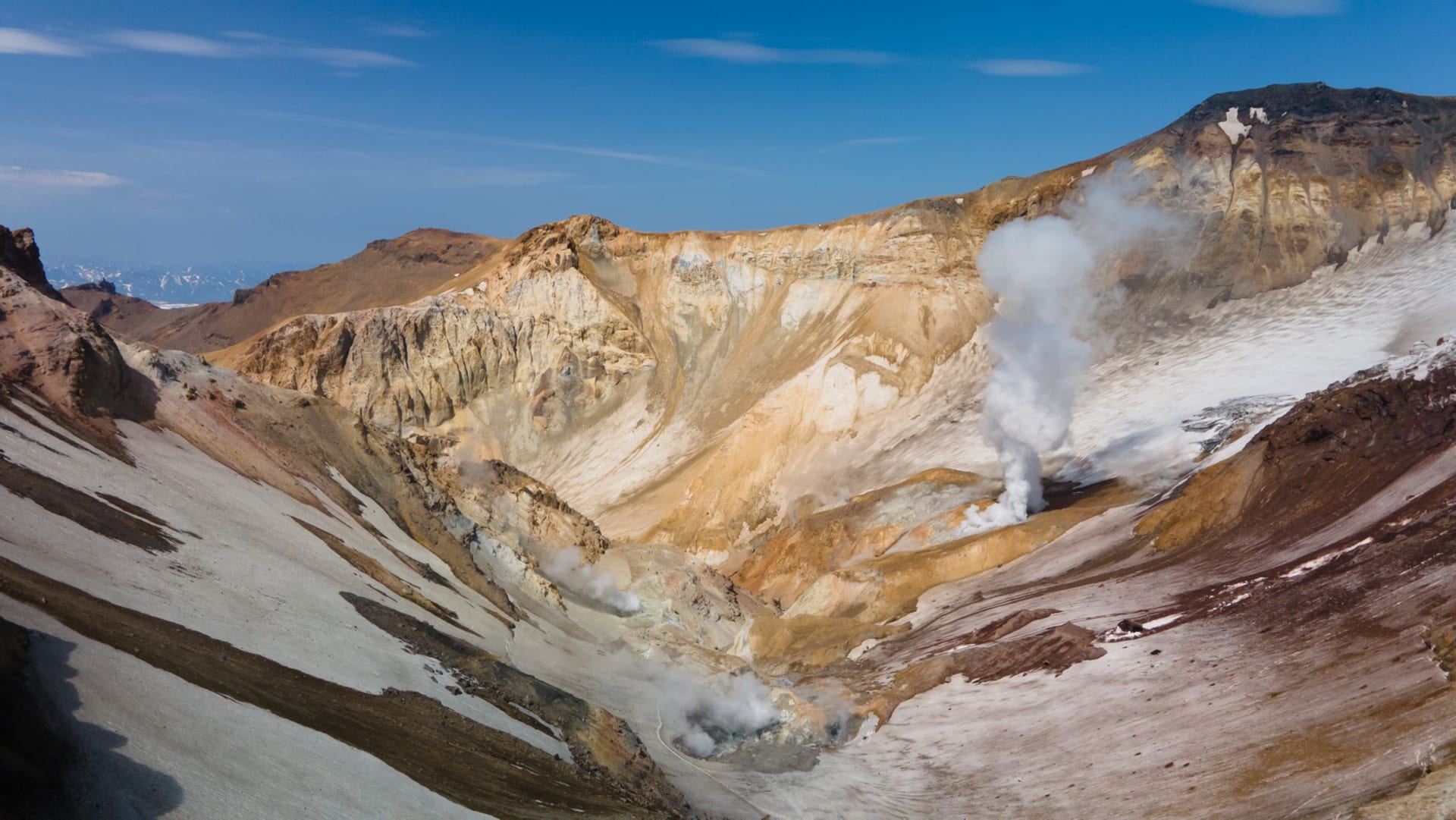 A geyser erupting against a dramatic volcanic landscape in Kamchatka, Russia