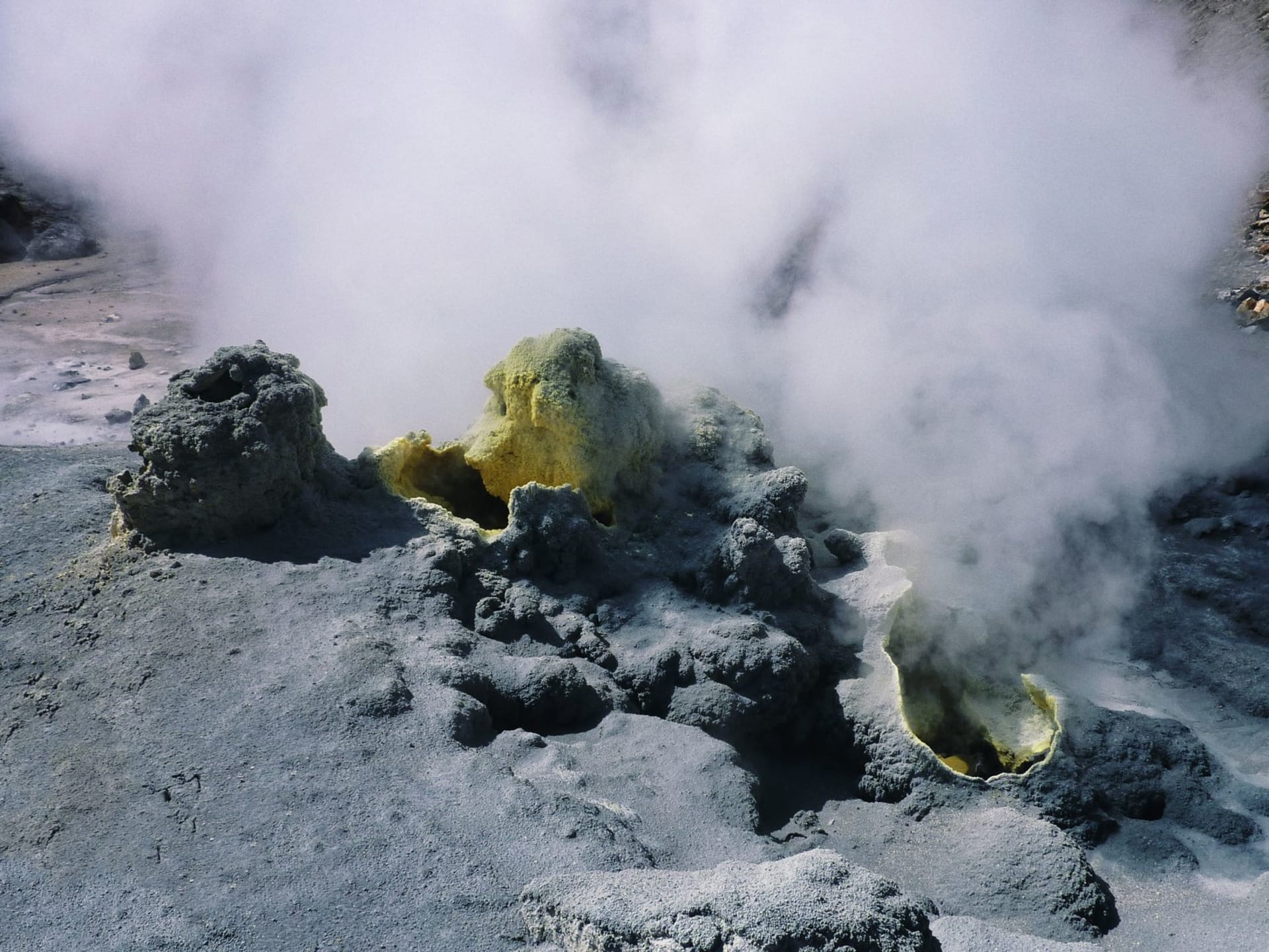 A natural thermal pool at Khodutka, southern Kamchatka, hot water steaming against the cold air, surrounded by tundra grass and distant volcanic peaks with no infrastructure in sight