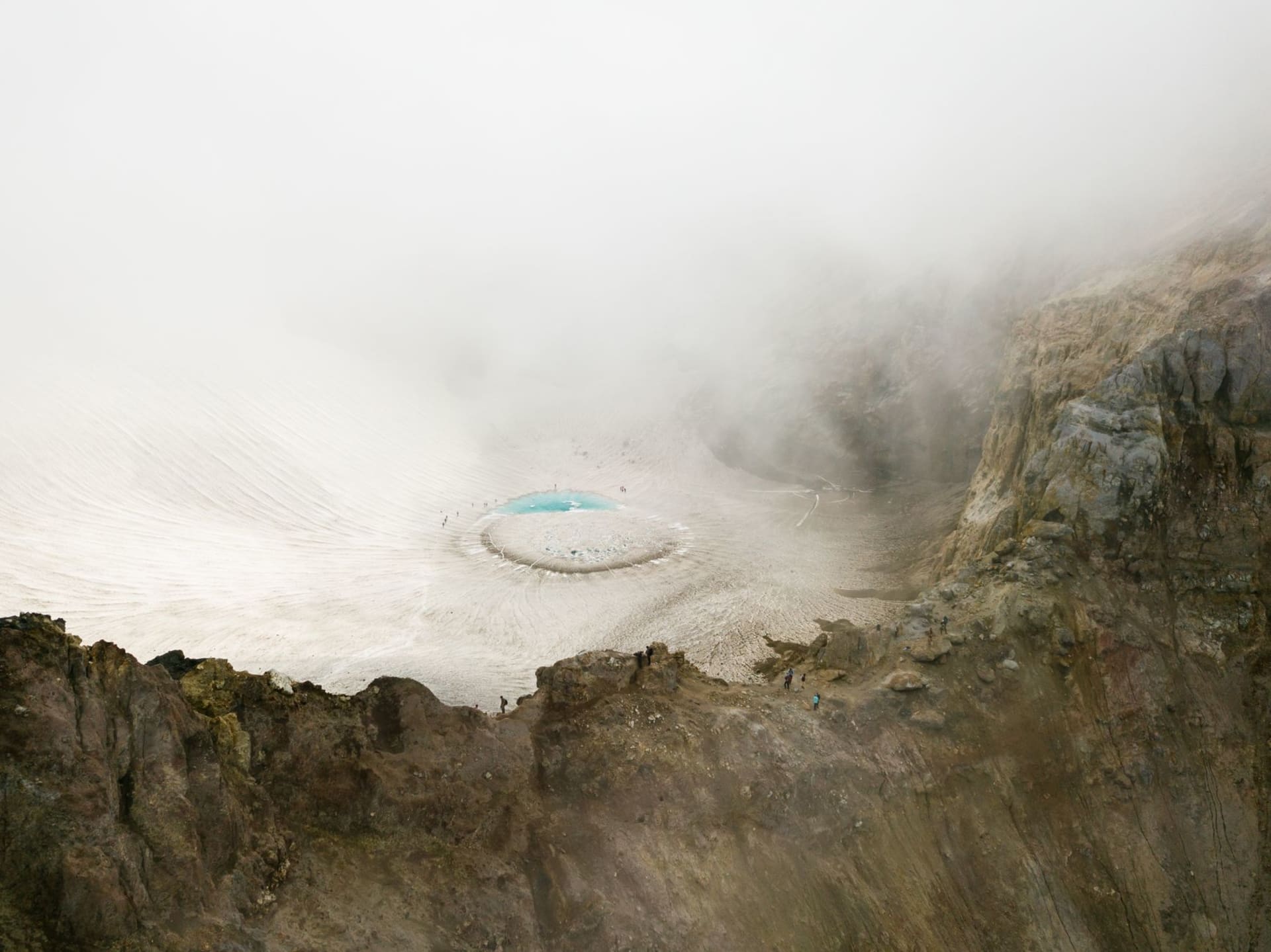 L'intérieur du cratère actif du volcan Mutnovsky, avec des dépôts de soufre jaune acide sur la roche grise, des fumerolles dégageant de la vapeur, et le bord d'un glacier s'effondrant au-dessus