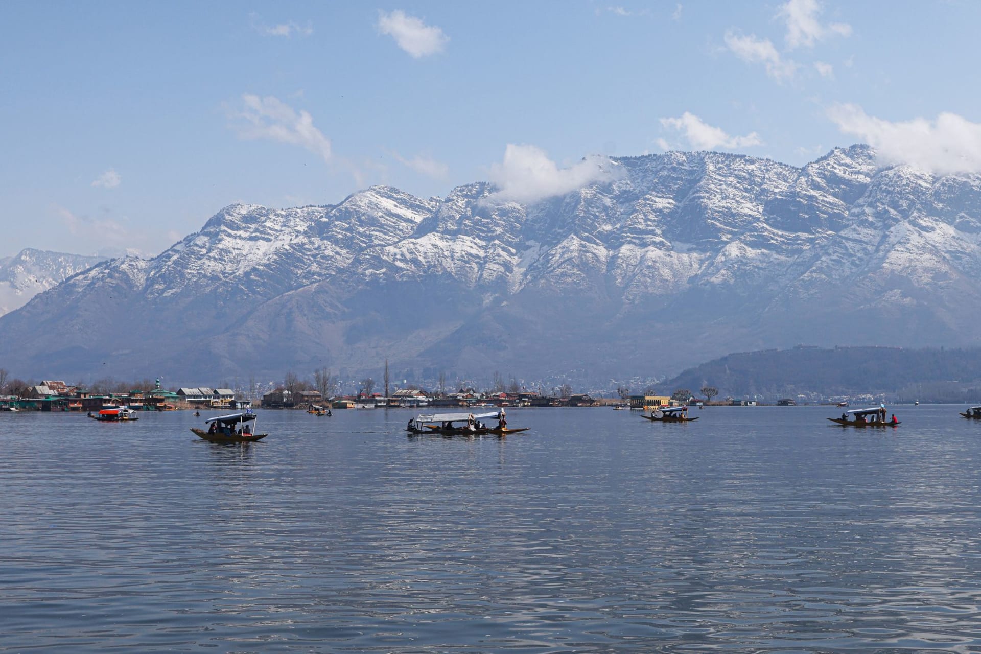 A shikara gliding across Dal Lake at dawn with mist rising and the Himalayan peaks reflected in glass-still water