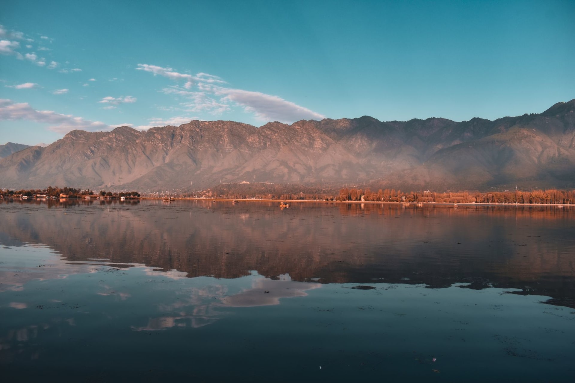 Wular Lake at dawn under a vast sky, flat grey water extending to the horizon with reed beds in the foreground and the Himalayan silhouette behind