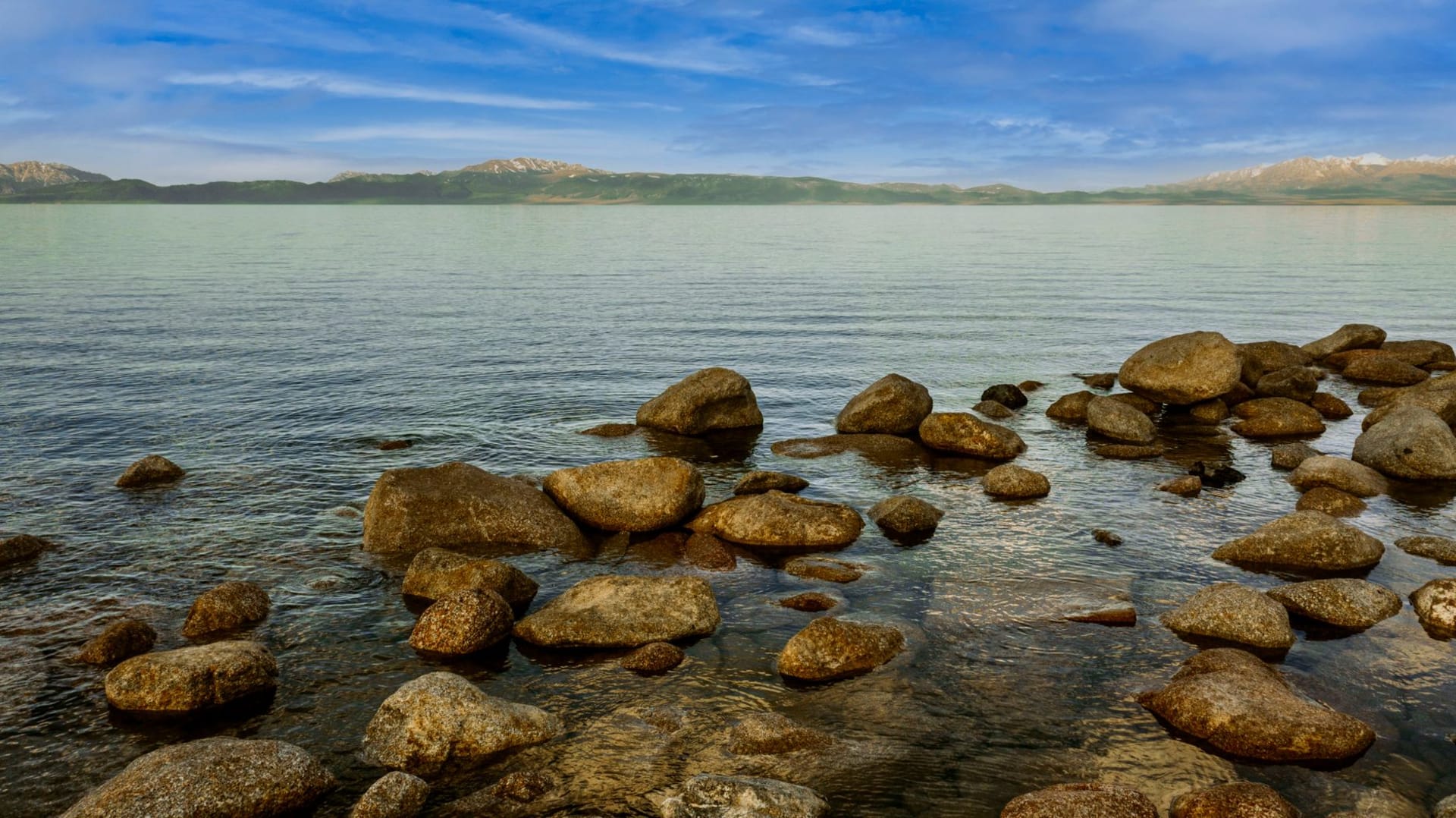 The vast shimmering expanse of Lake Balkhash stretching to the horizon under a dramatic sky, its waters shifting from turquoise to deep blue near the industrial shore