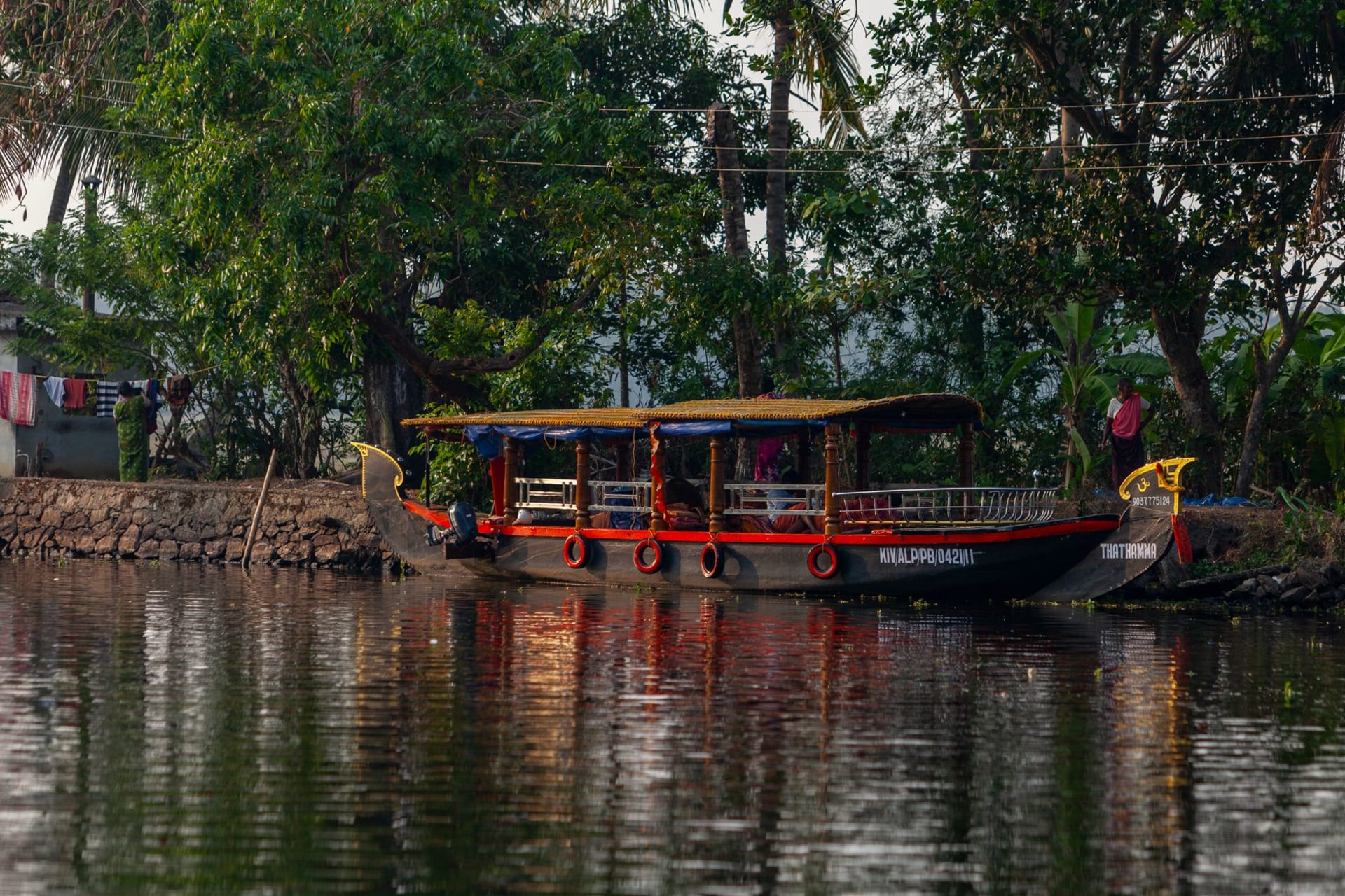 Traditional Kerala kettuvallam houseboat gliding through palm-lined canals at golden hour with still amber water
