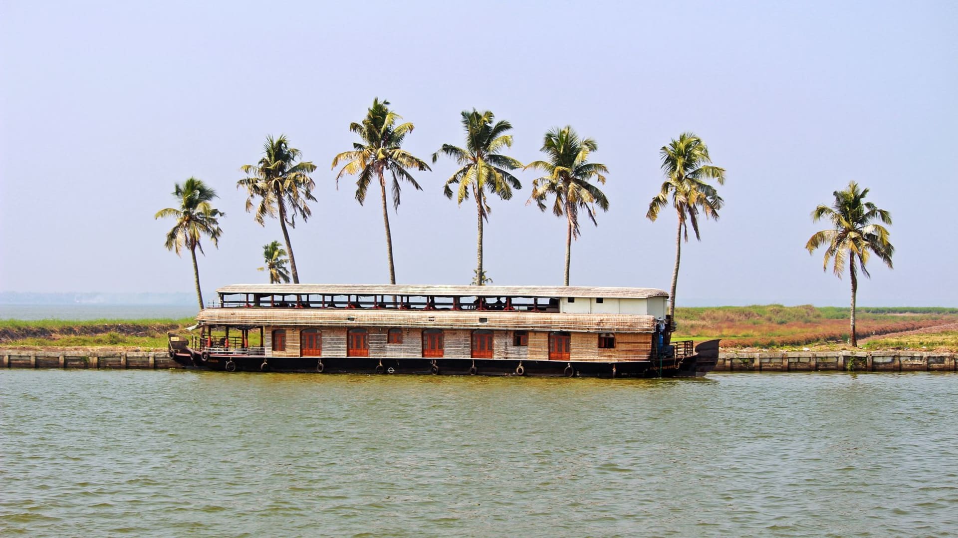Traditional Kerala houseboat gliding through the calm backwaters beside tall coconut palms under a clear sky