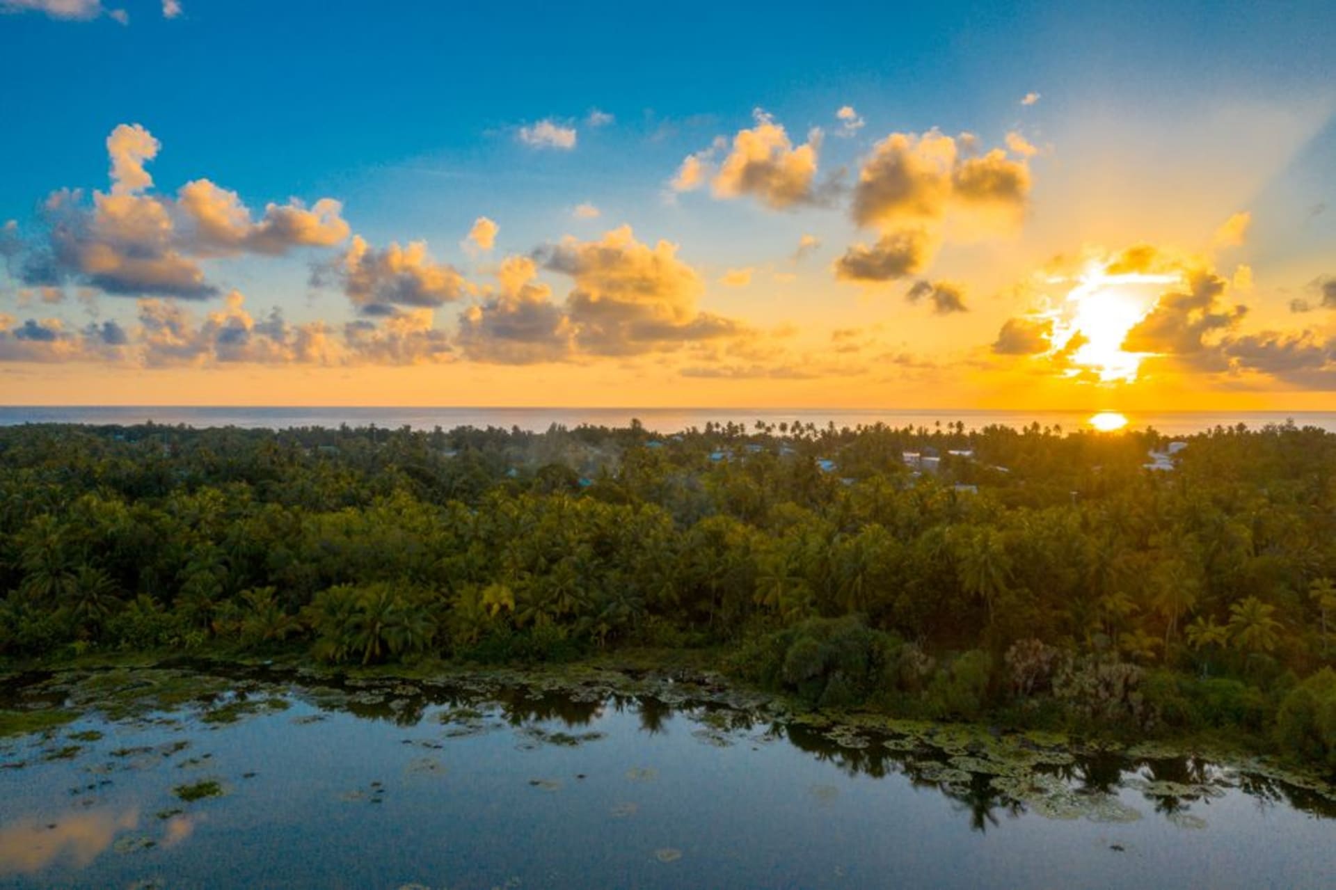 Amplia laguna turquesa en el atolón Tabuaeran bordeada de denso bosque de palmeras cocoteras, con un canal estrecho conectando hacia el océano abierto
