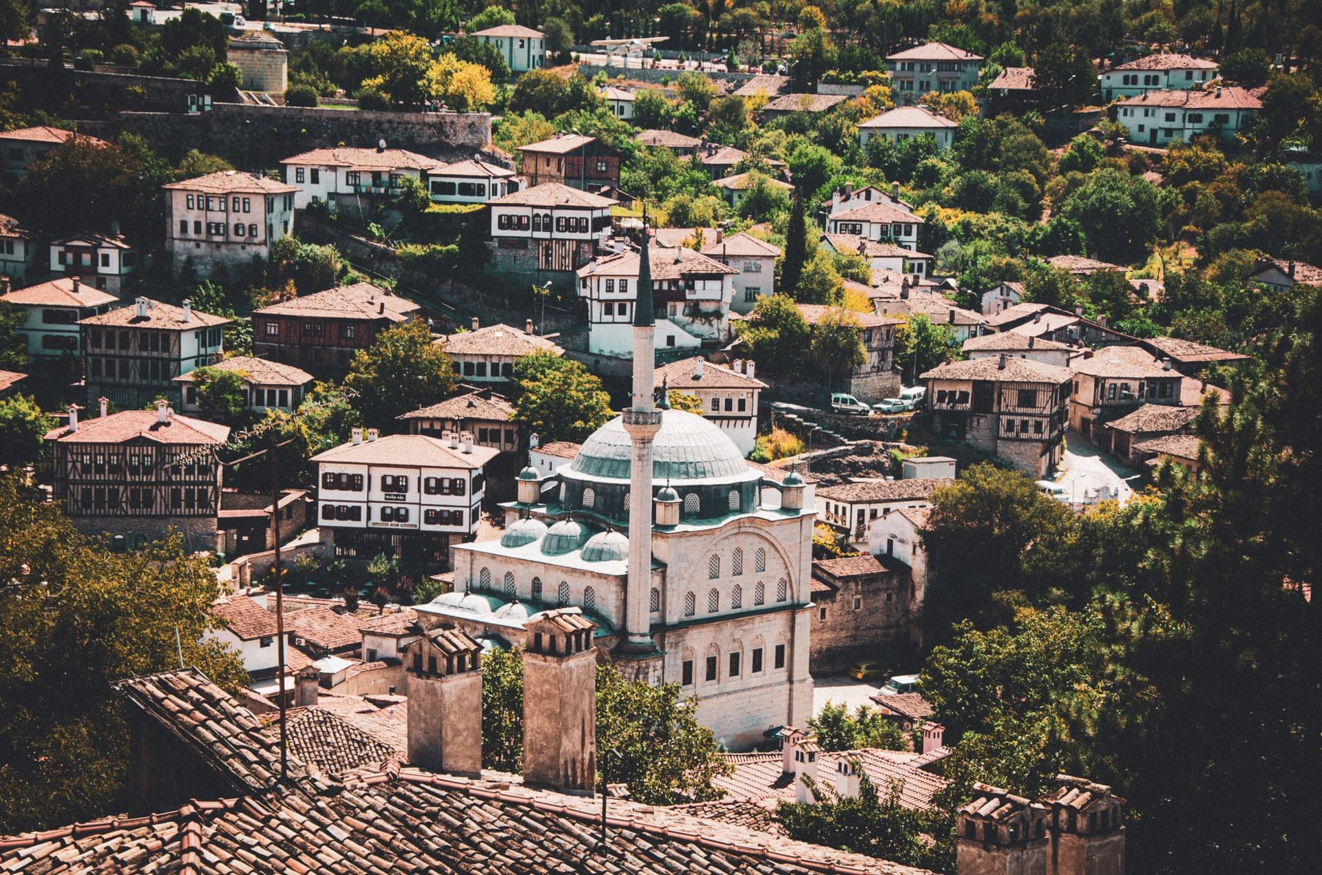 Prizren's Ottoman stone bridge over the Bistrica River with minarets and red-roofed houses rising behind at golden hour