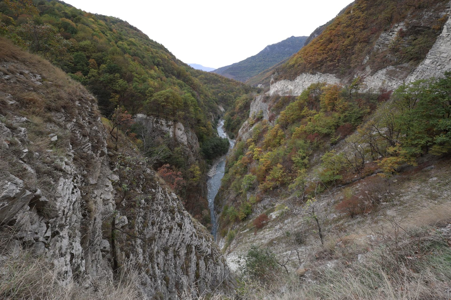 A narrow road threading through sheer limestone walls of Rugova Canyon with a turquoise river far below in morning light