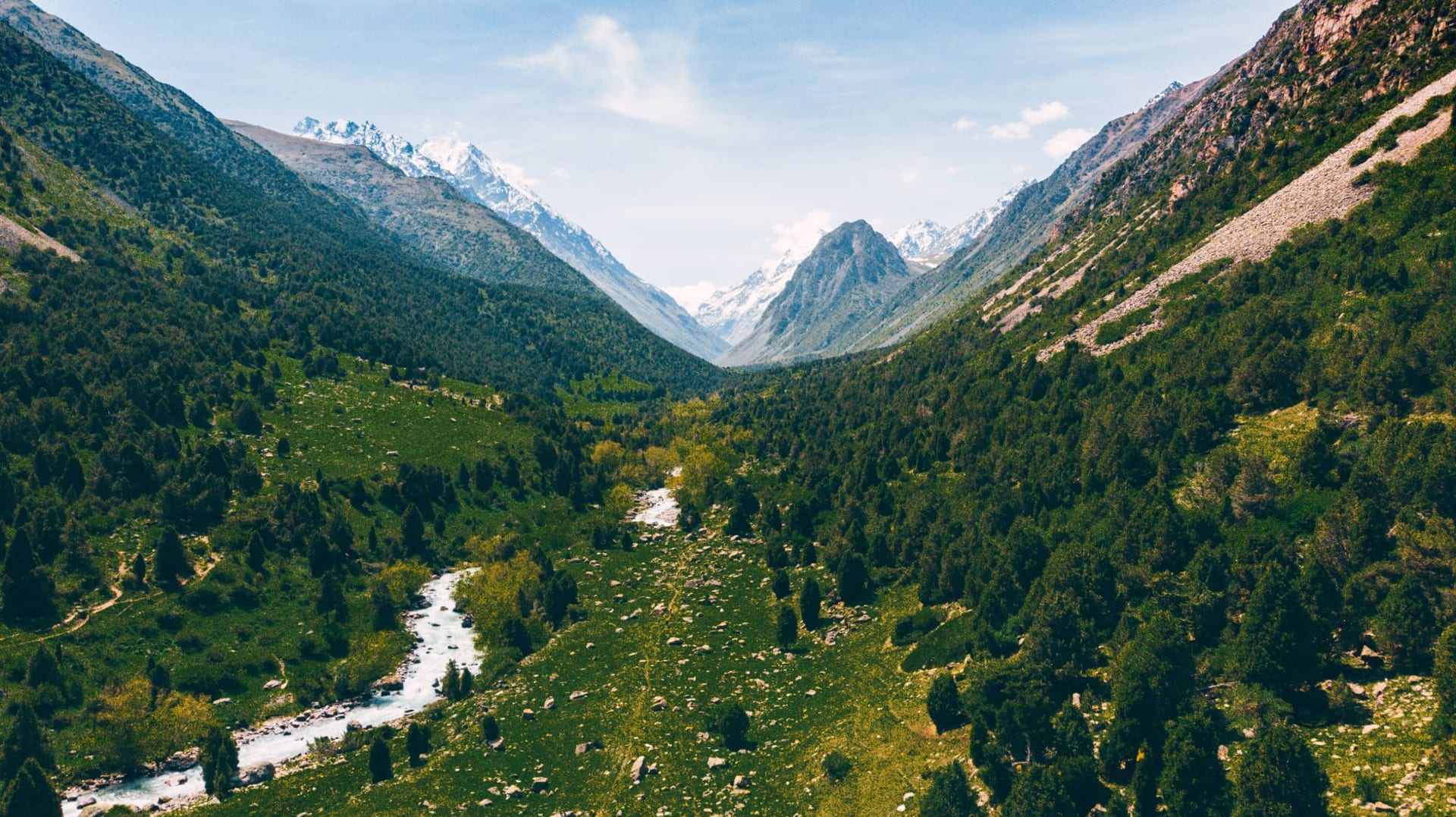 Rocky glacial gorge in Ala Archa with a torrent of grey-white water and jagged snow-covered peaks rising above
