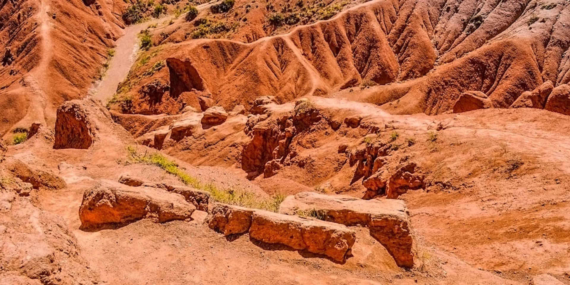 Formaciones de arenisca roja y naranja del Cañón de Skazka elevándose sobre la orilla del lago Issyk-Kul