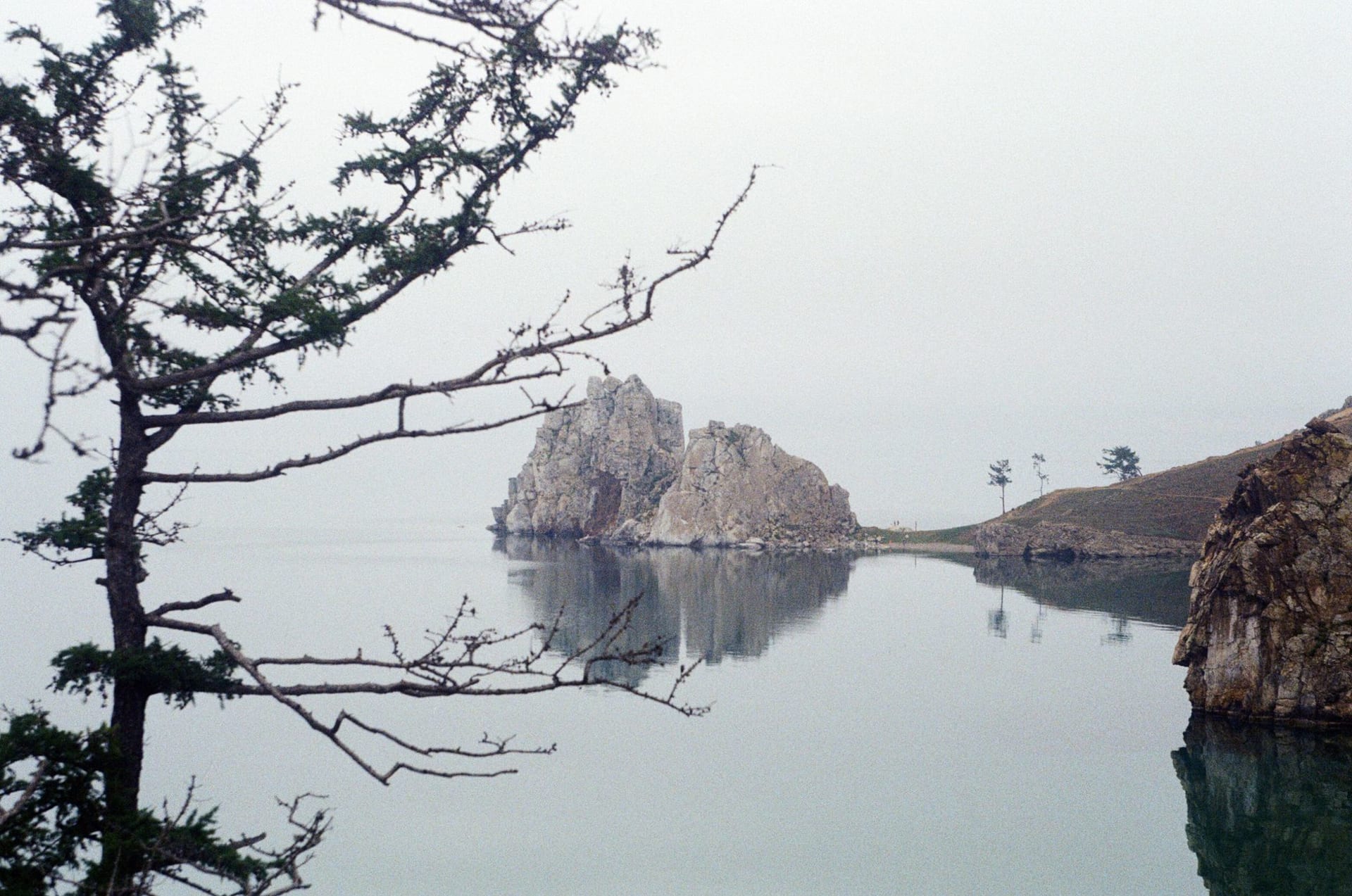 A handful of wooden cabins at the edge of the taiga forest with the glassy surface of Lake Baikal directly below, no road visible