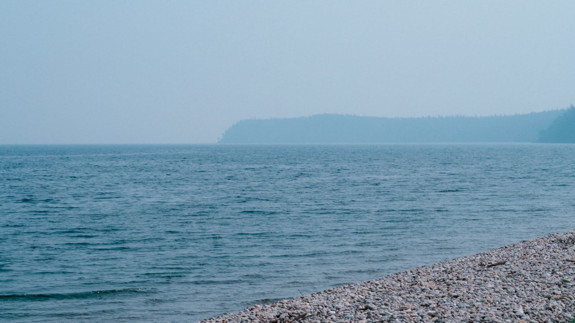 A lone vehicle crossing the vast white frozen surface of Lake Baikal toward Bolshoe Goloustnoe, mountains visible on the far shore