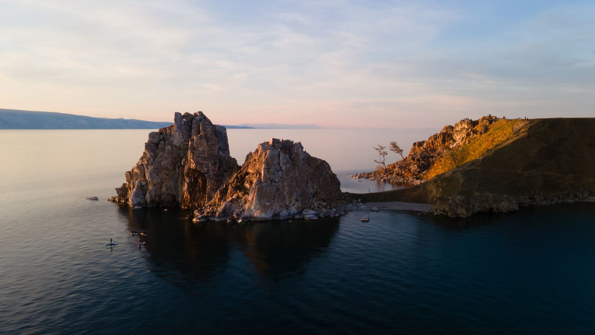 Burkhan Rock's two marble pillars rising from the frozen surface of Lake Baikal at dawn, ice stretching in every direction