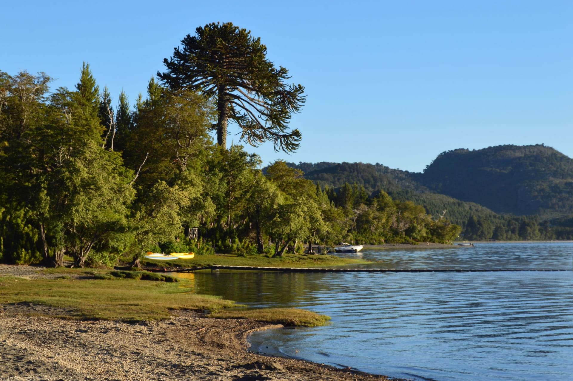 The pier and wooden waterfront of Villarrica town at sunset with the smoking cone of Villarrica volcano reflected in the calm lake
