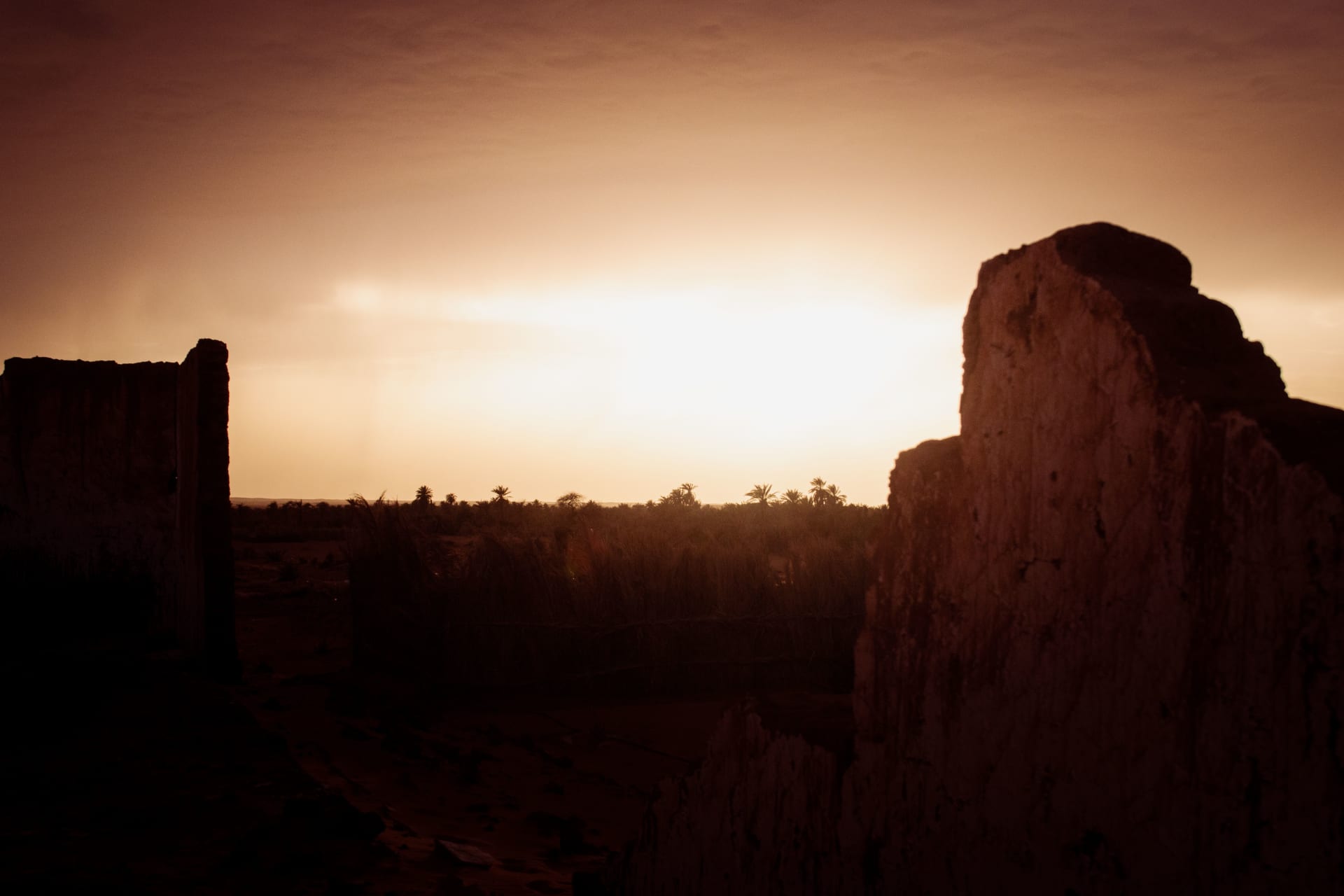 Silhouette of ancient ruins against a glowing desert sunset, columns and arches backlit by orange and violet sky