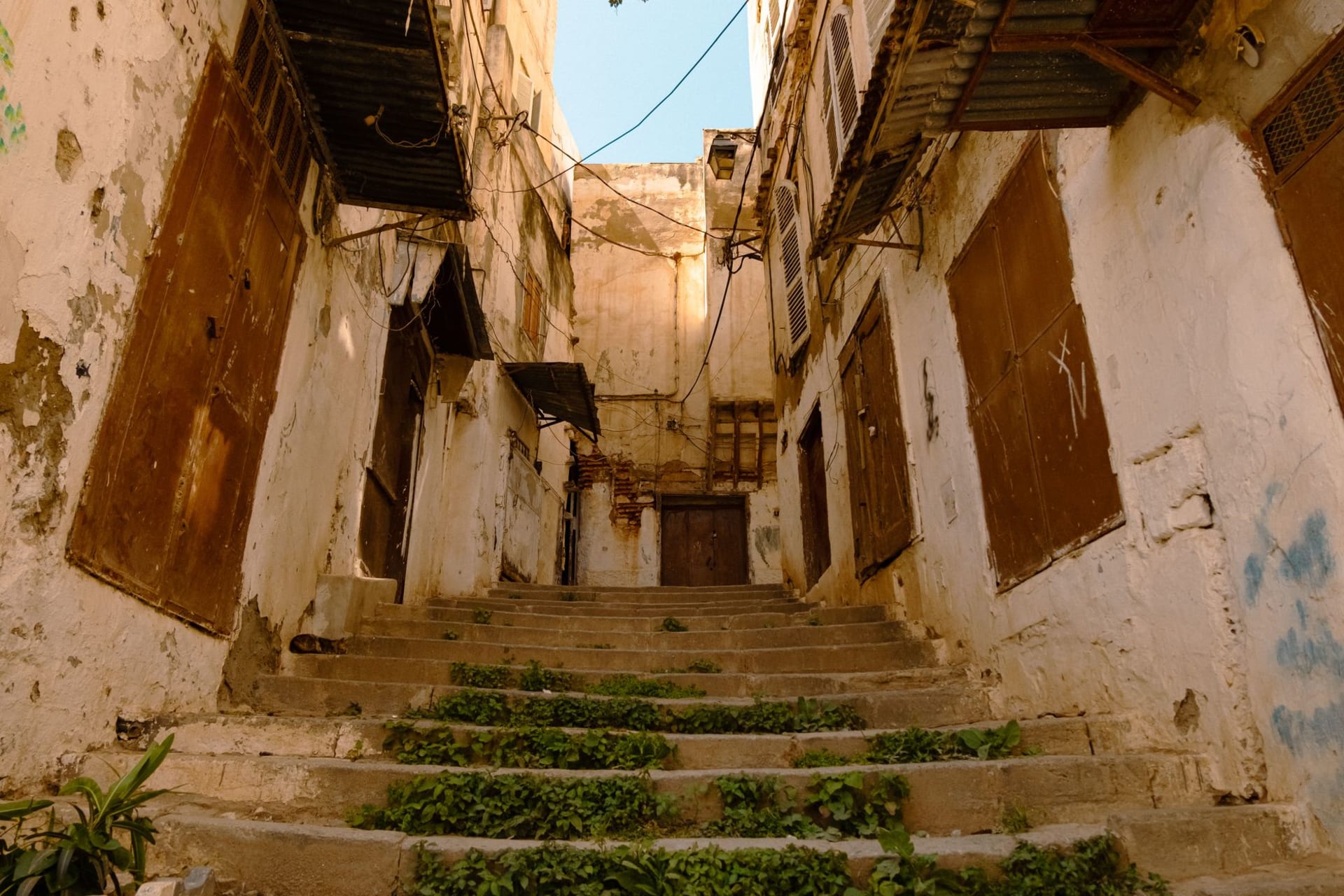 The Arch of Marcus Aurelius rising above Tripoli's old city streets, white-washed buildings flanking the ancient marble triumphal arch under a clear blue Mediterranean sky