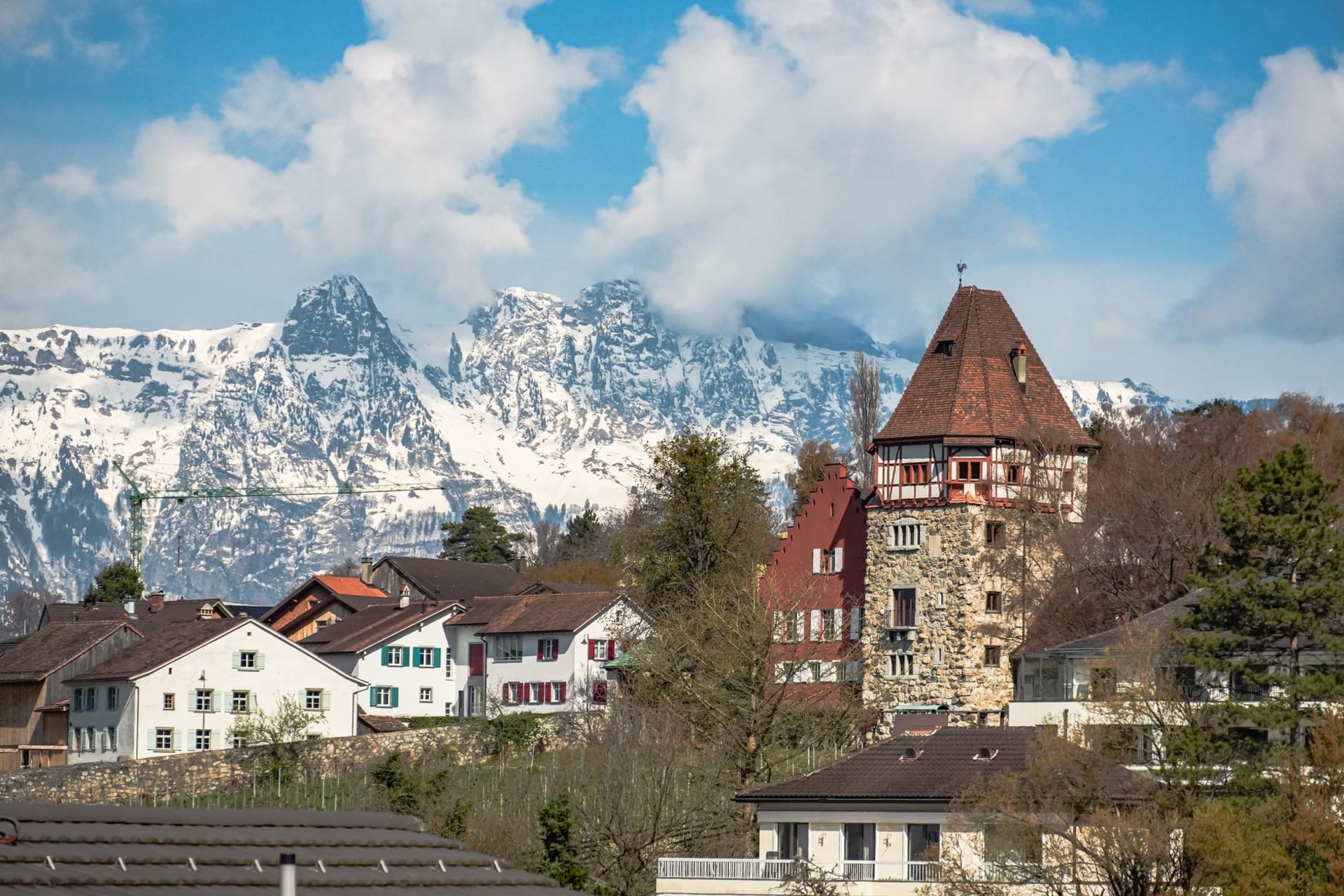 Planken village on its narrow mountain terrace, traditional farmhouses with the Rhine valley spread far below and the Swiss Alps on the horizon