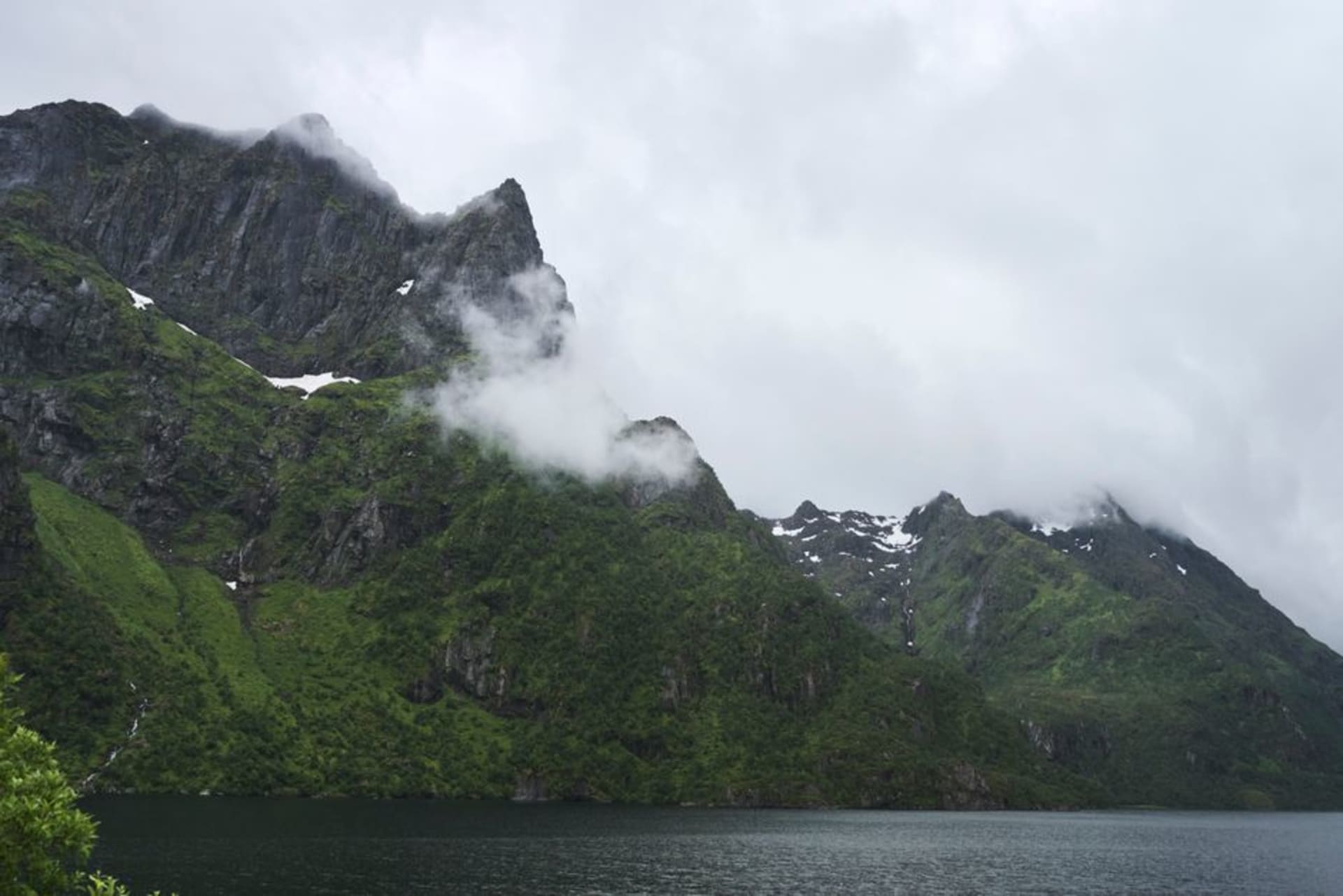 Steep rock walls of Trollfjord rising directly from calm dark water under an overcast Arctic sky