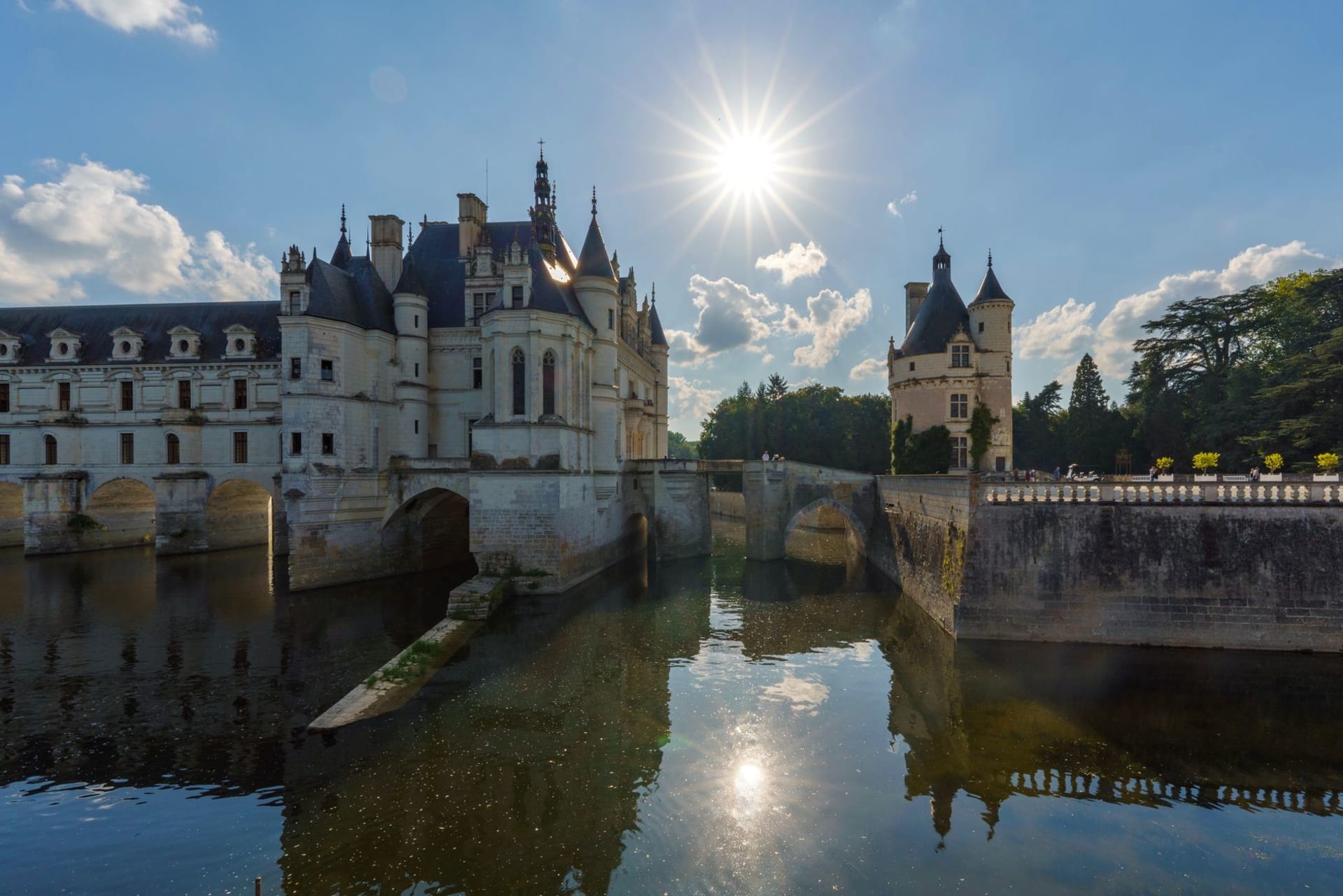 A white Renaissance château spanning a calm river on a series of stone arches, reflected in the water