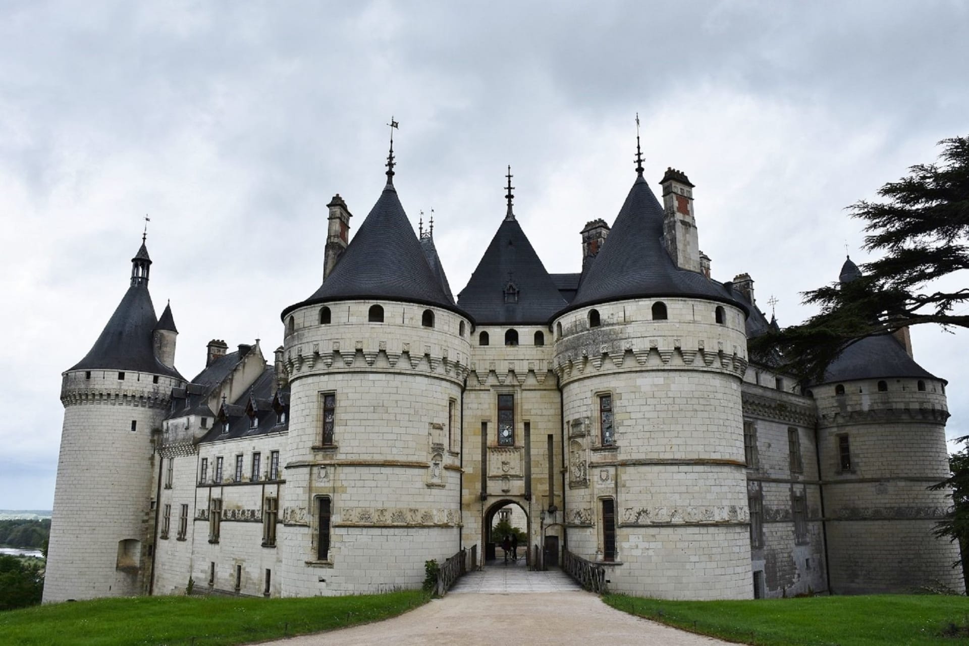 The white tuffeau façade of Château de Cheverny under a blue sky, its classical symmetry framed by formal gardens and parkland beyond