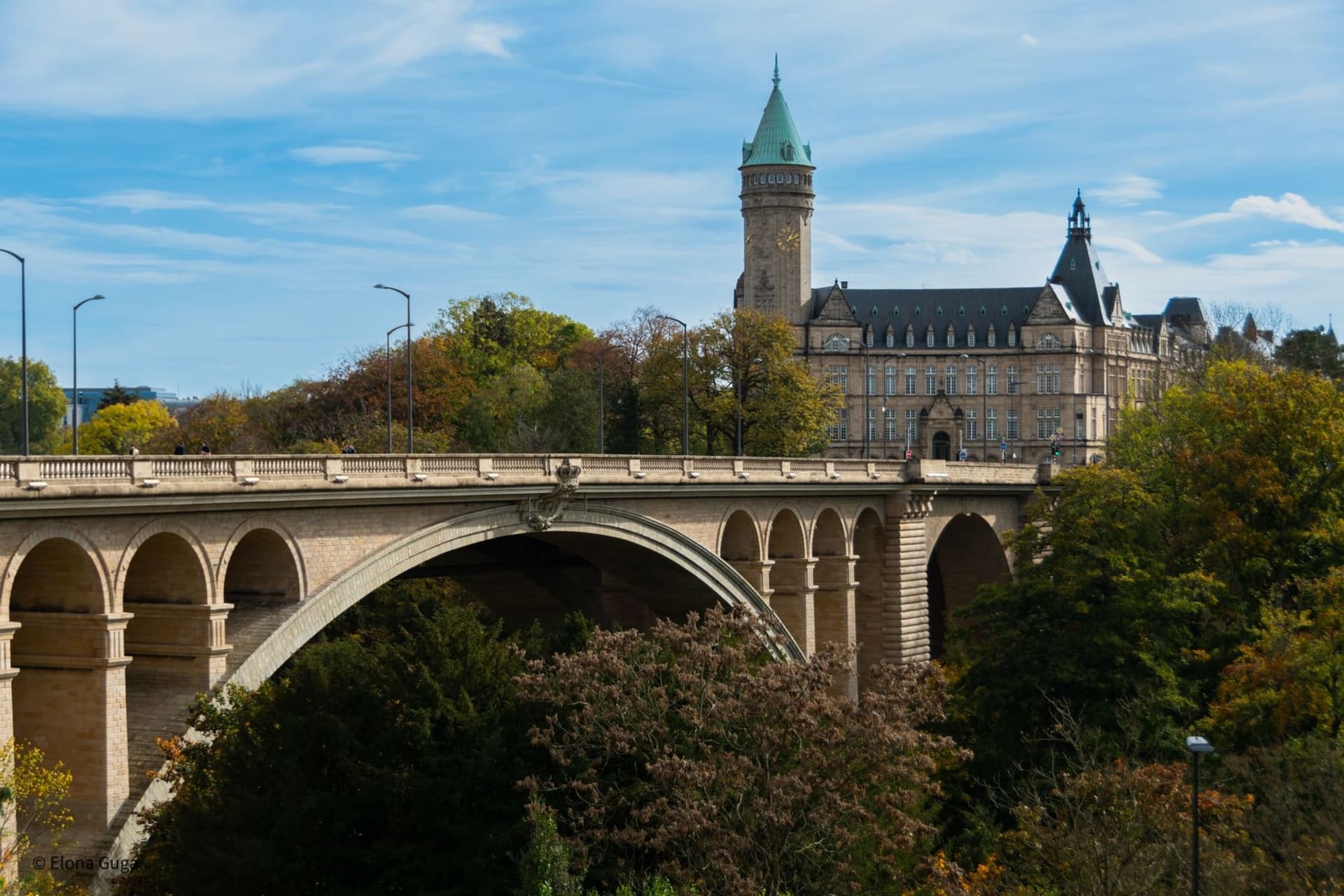 Stone ramparts and medieval towers of the Bock Casemates rising above the deep green gorge of the Alzette river, with the old city skyline stretching beyond in afternoon light.