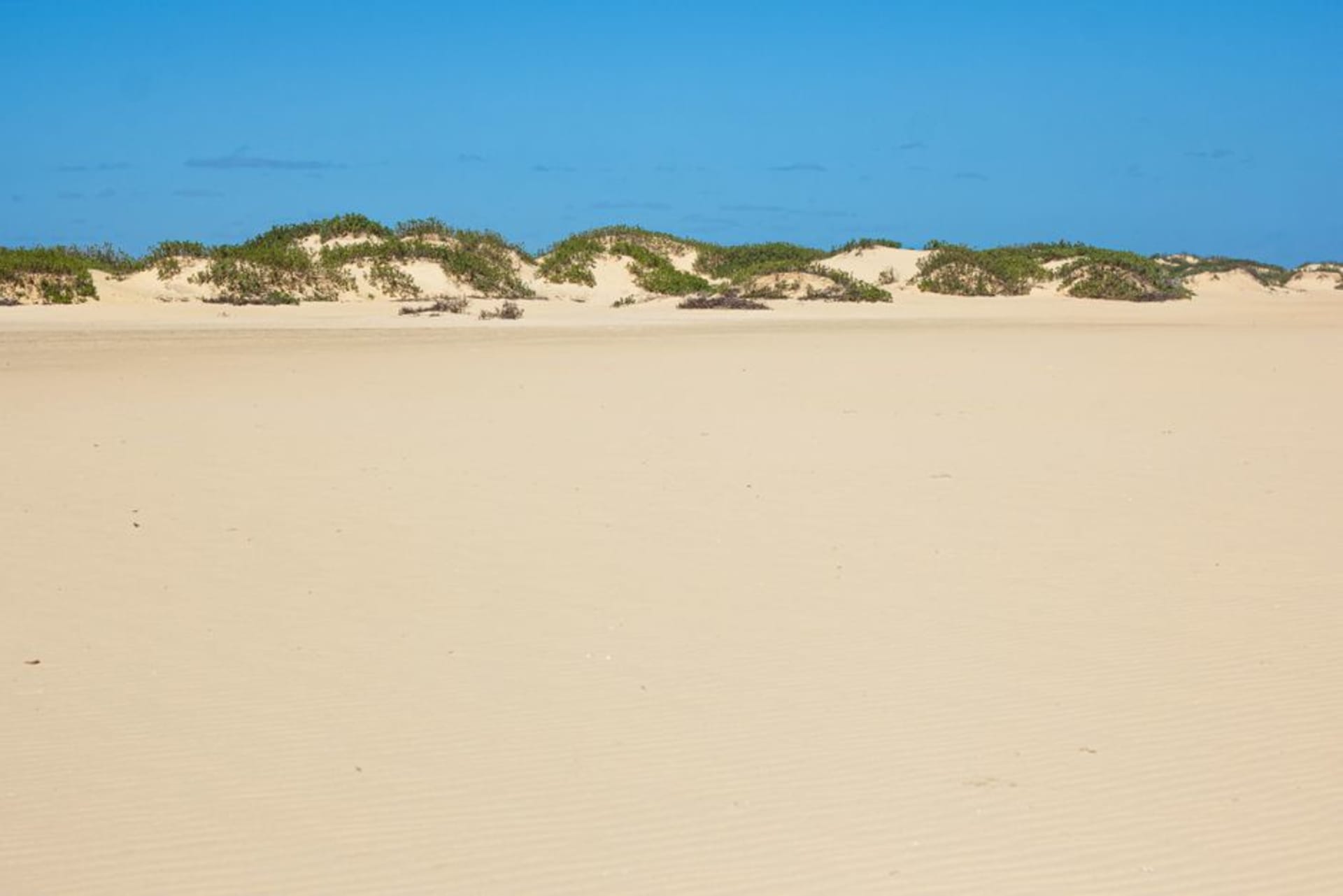 A crescent of white sand dunes rising behind the fishing village of Anakao, with traditional sailing pirogues drawn up on the beach