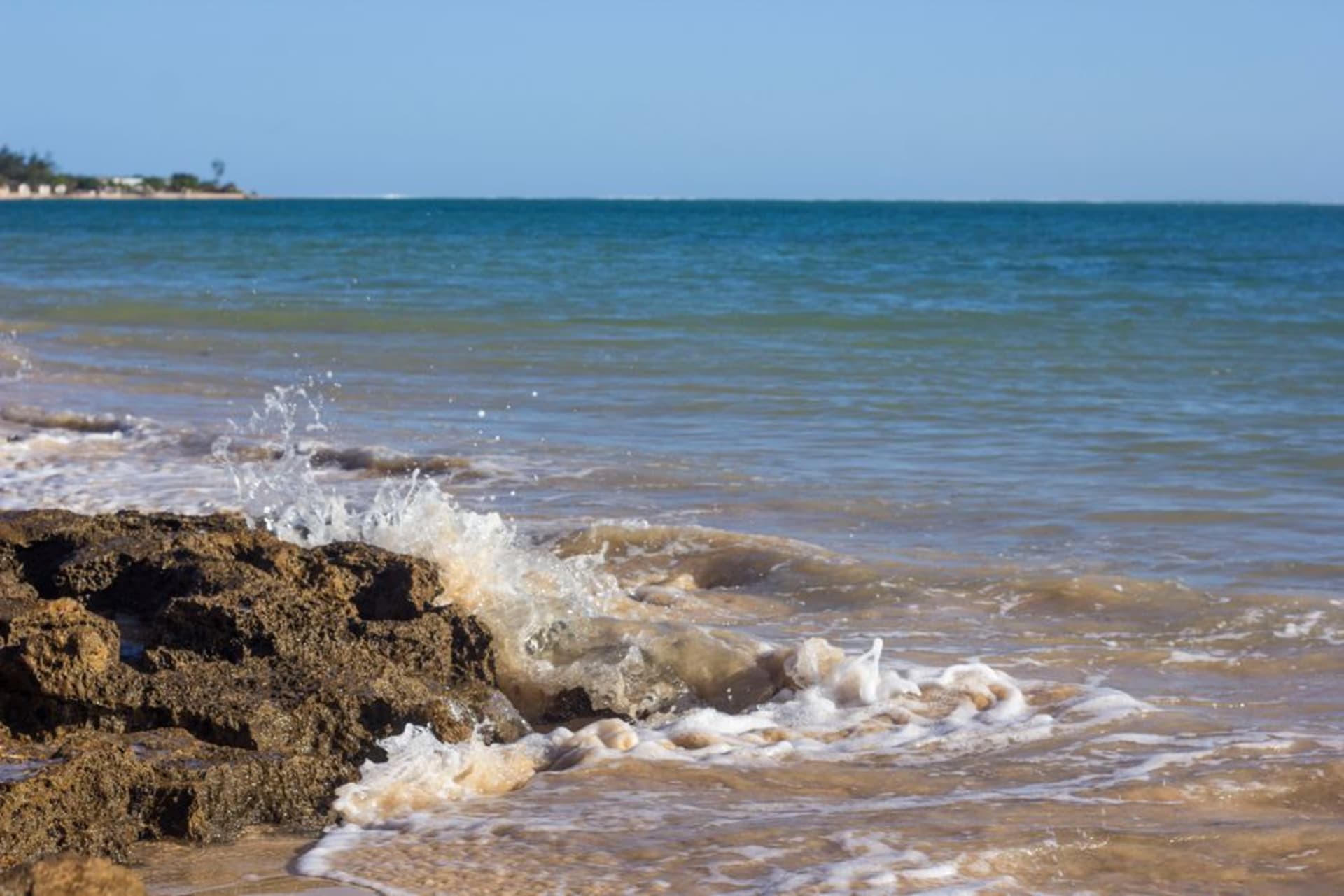 Une plage de sable blanc à Ifaty bordée de palmiers et de simples bungalows de plage, une eau turquoise calme et une ligne de récif visible au loin