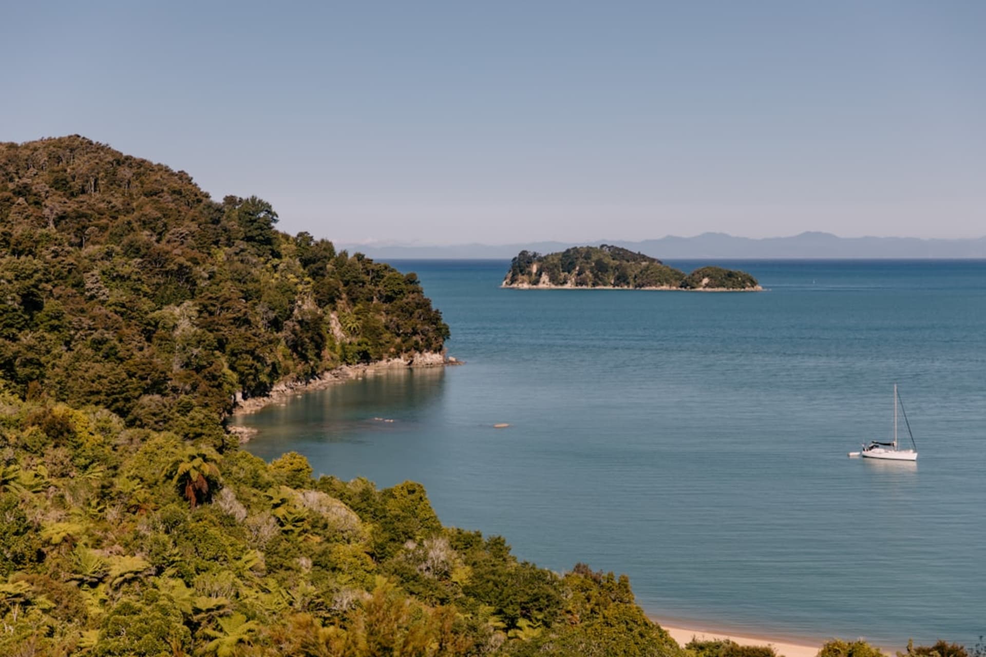 Une plage de sable blanc sur l'île de Nosy Tanikely, un phare visible sur le promontoire au-dessus et une eau turquoise bordée de récif corallien