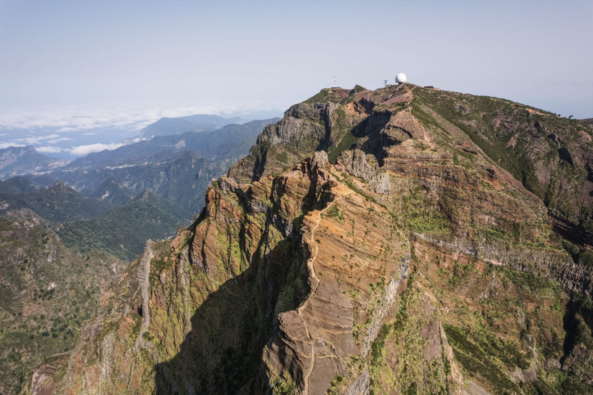 Hikers on the rocky summit ridge of Pico Ruivo above a sea of cloud, volcanic peaks emerging in early morning light
