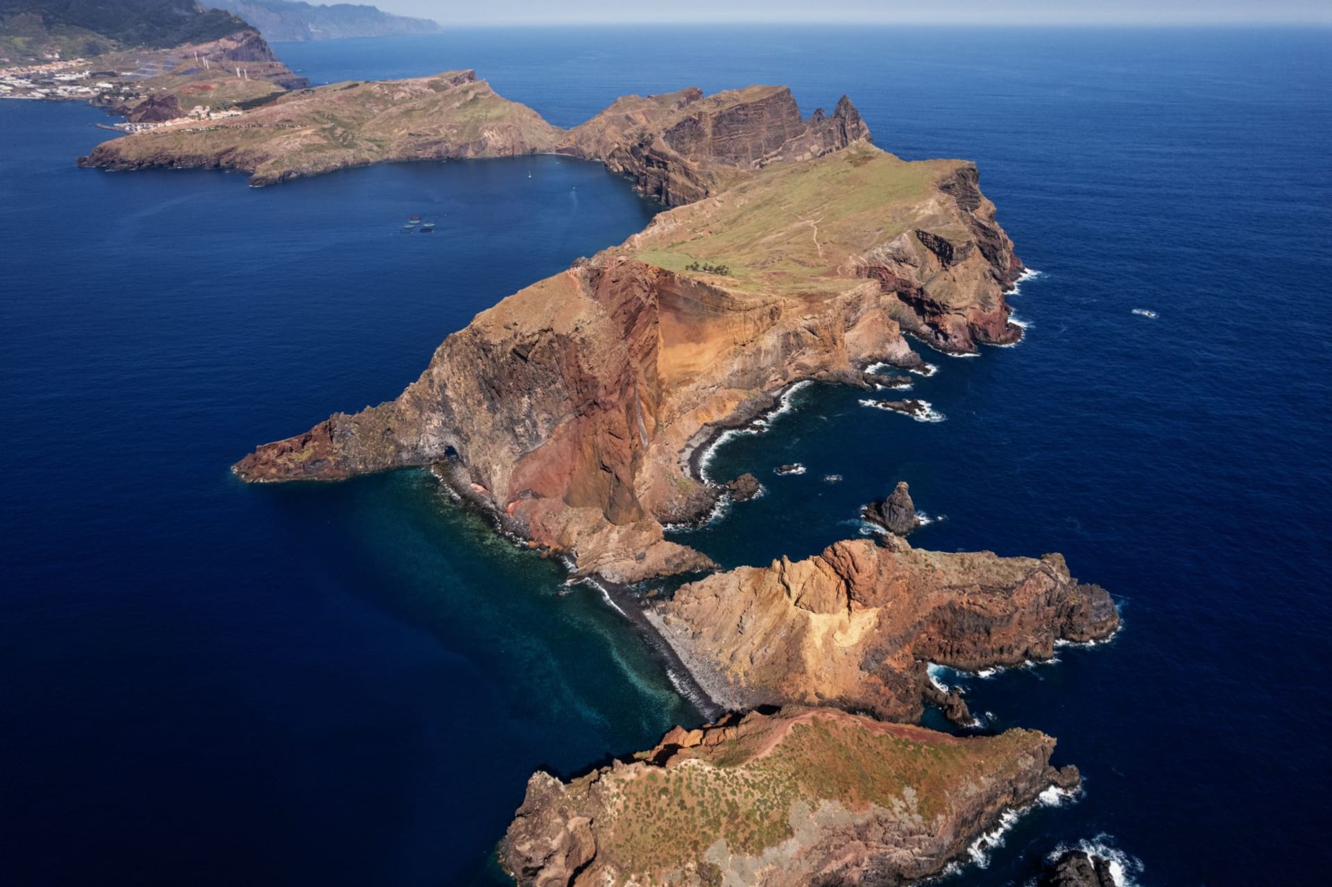 A bare red and ochre peninsula of jagged rock stretching into a deep blue ocean