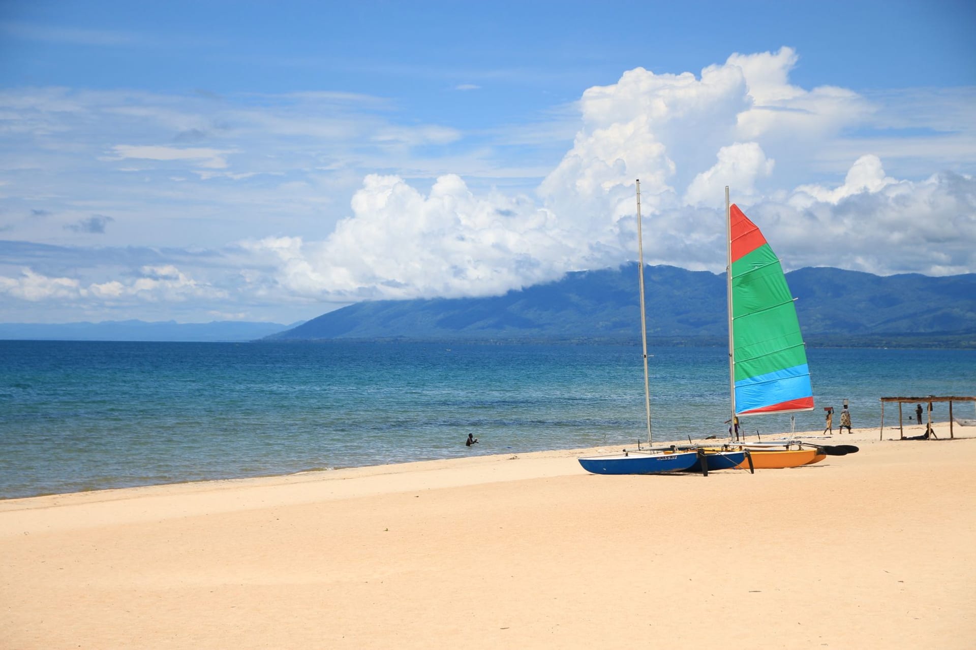 A wide stretch of deserted white sand beach at Senga Bay, Lake Malawi glassy at low sun with distant purple hills