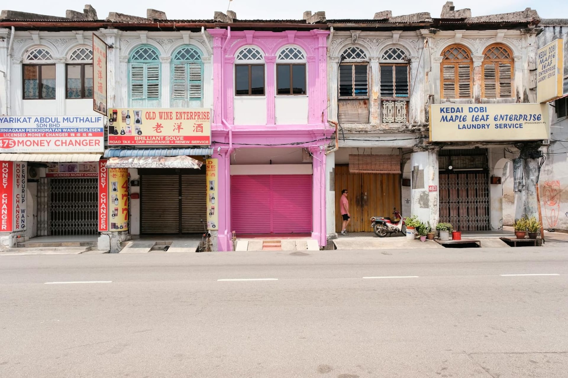 A cyclist rides past a large-scale mural painted on the weathered wall of a colonial shophouse in George Town, Penang, the artwork depicting local children playing against faded ochre plaster.