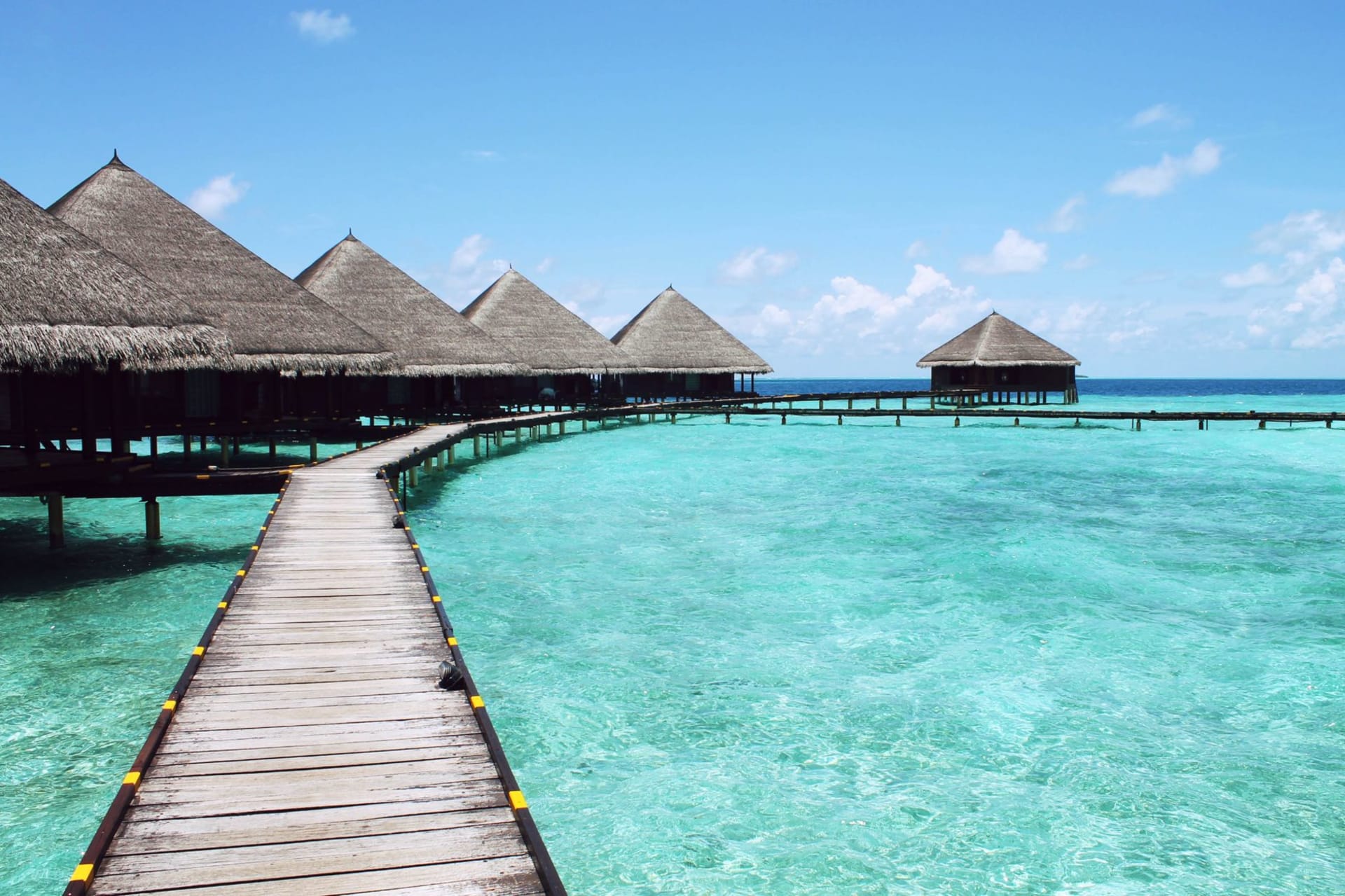 Overwater bungalows on stilts above a calm turquoise lagoon, photographed from above at the Maldives