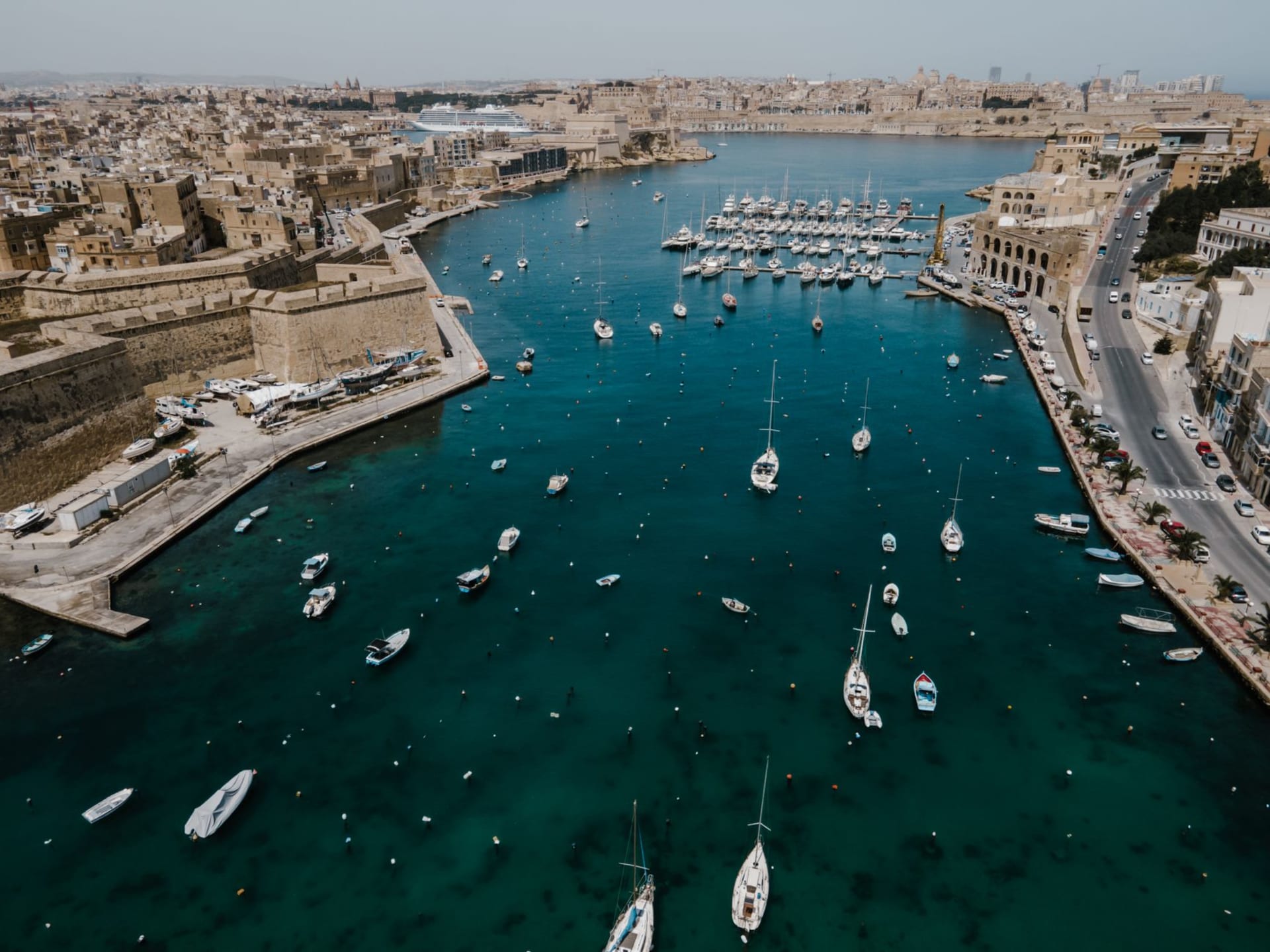 Birgu waterfront at dusk with Fort St. Angelo rising above the marina and Valletta glowing across the Grand Harbour