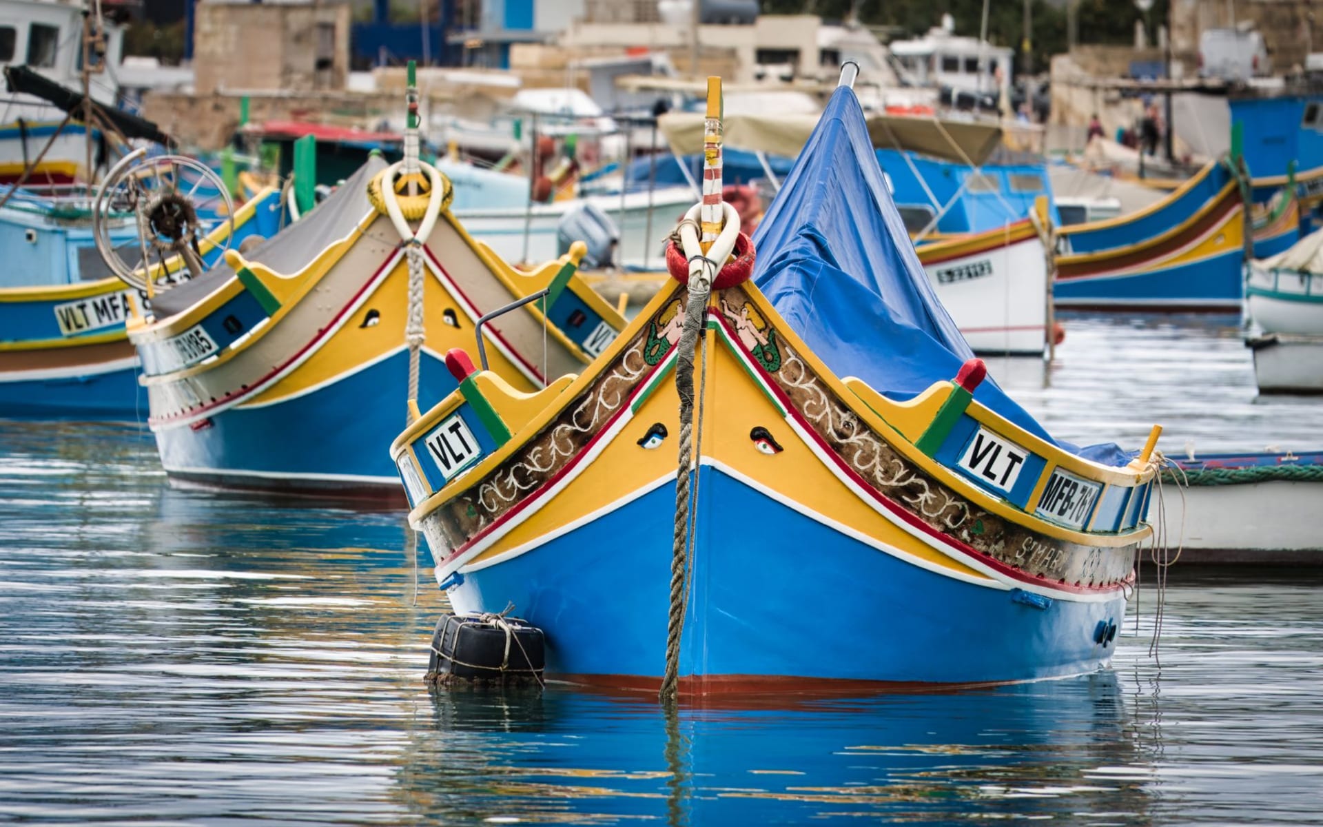 Colorful traditional luzzu fishing boats with painted eyes moored in Marsaxlokk harbor at golden hour