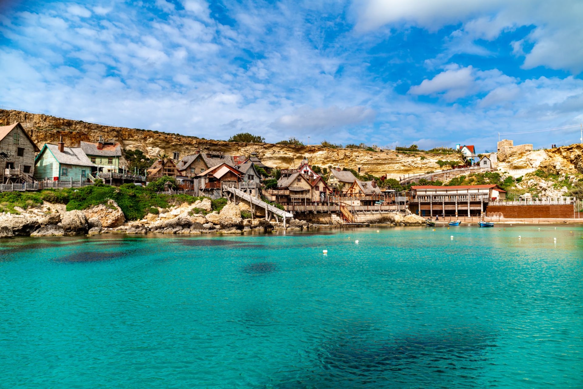 Mellieha Bay's wide sandy beach curving along calm turquoise water with the Mellieha hillside town rising behind