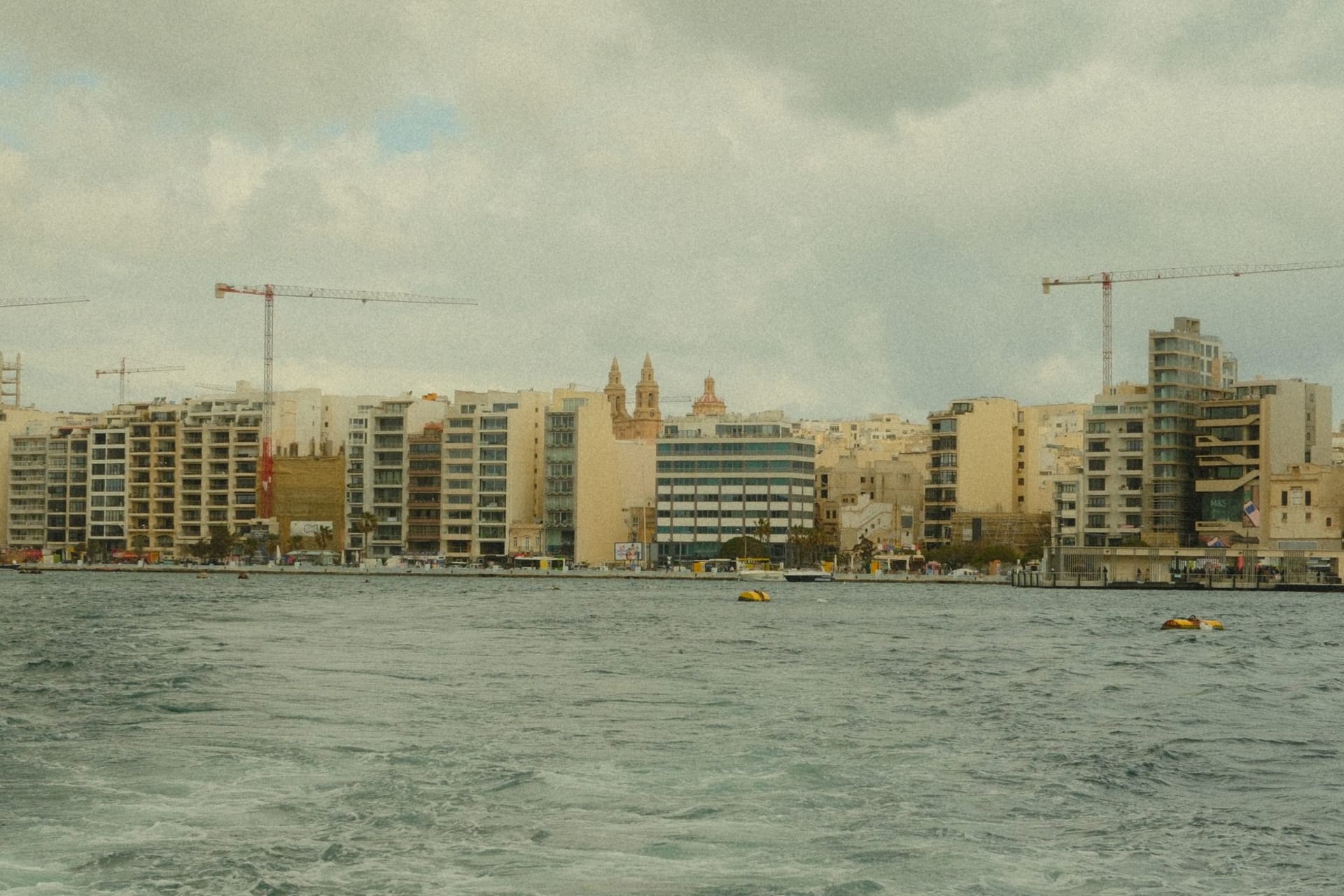 Sliema seafront promenade at golden hour with Valletta's bastions visible across the water and locals walking the flat limestone waterfront