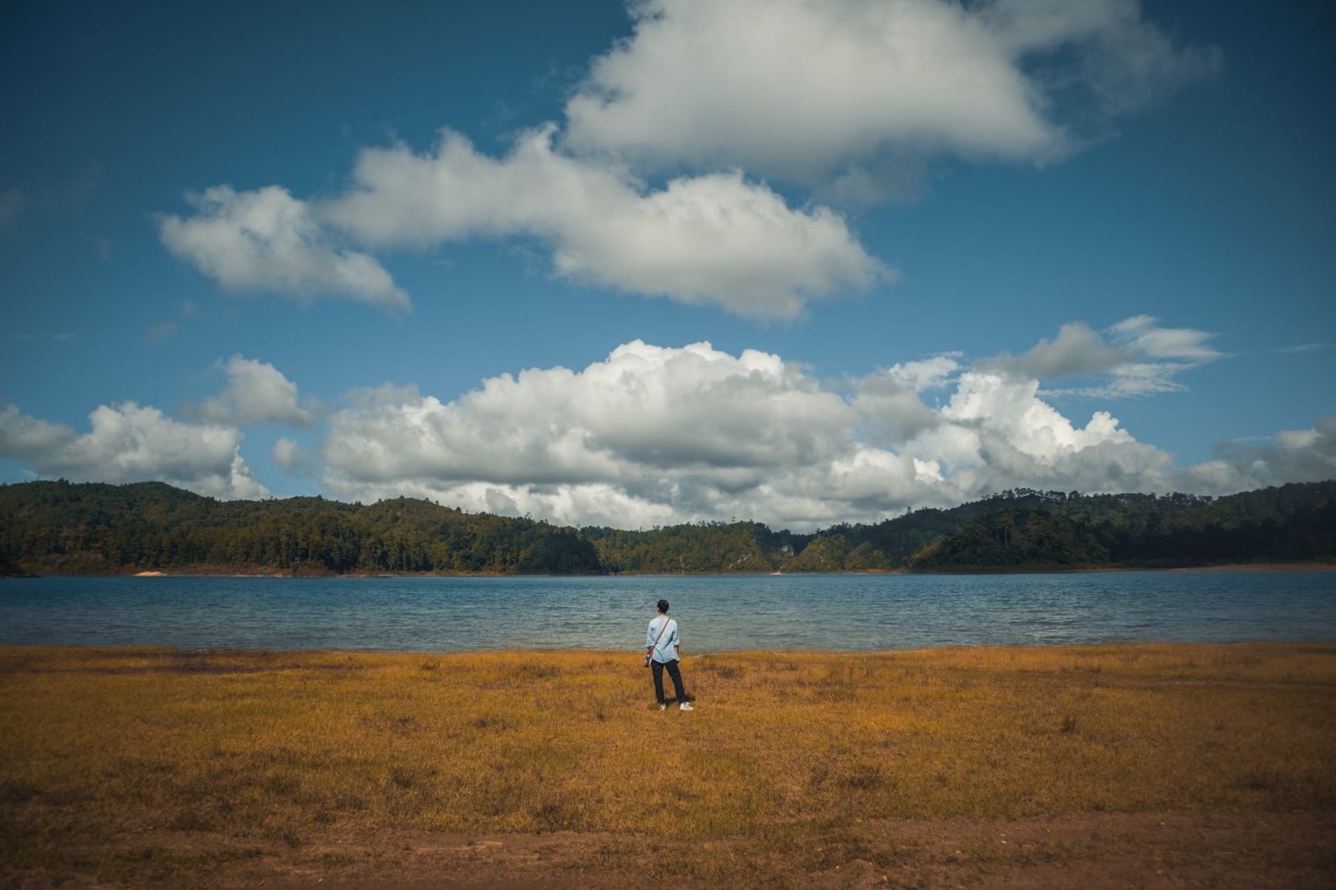 Umiam Lake at golden hour, pine-covered hills reflected in still water, a single wooden boat anchored near the far shore