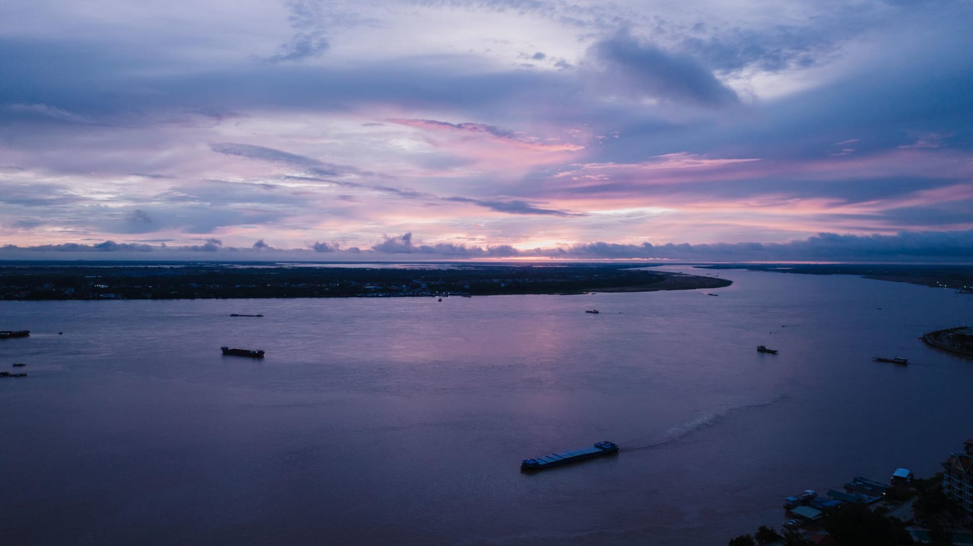 A hillside village of wooden stilted houses above the Mekong River at dusk, lights beginning to flicker on