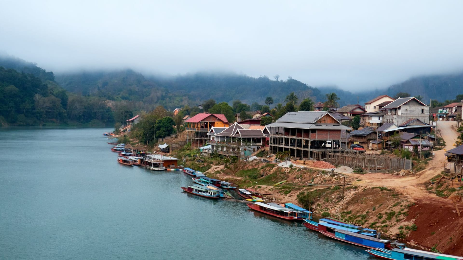 The dark mouth of Tham Ting cave set into a limestone cliff above the Mekong River, boats moored below