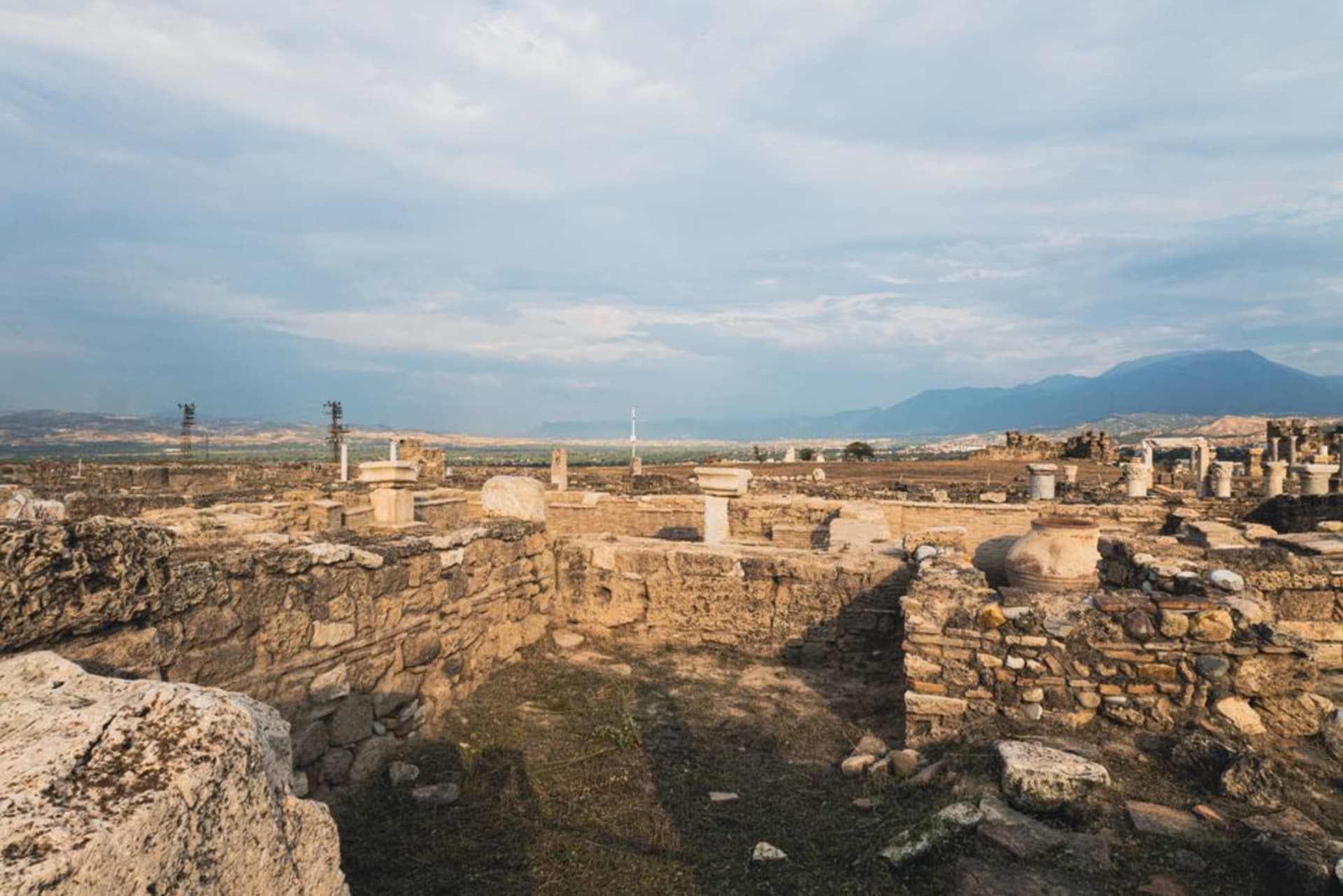 Les ruines érodées en brique crue de la ziggurat d'Anu à Uruk s'élevant sur une étendue plate de sable et de tessons de poterie dispersés sous un ciel désertique pâle