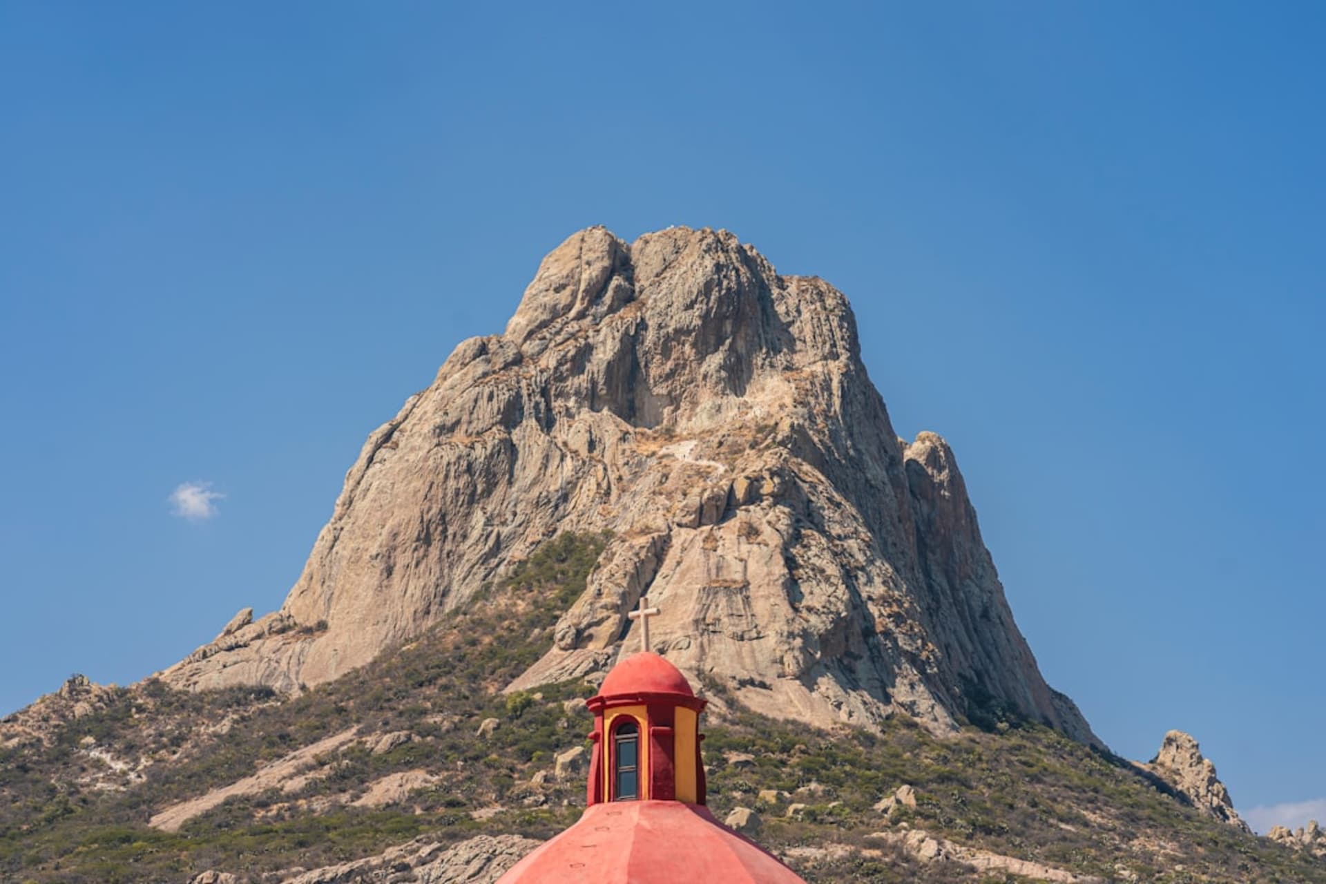 The Peña de Bernal monolith rising over the terracotta rooftops of the pueblo of Bernal, Querétaro, in warm late-afternoon light