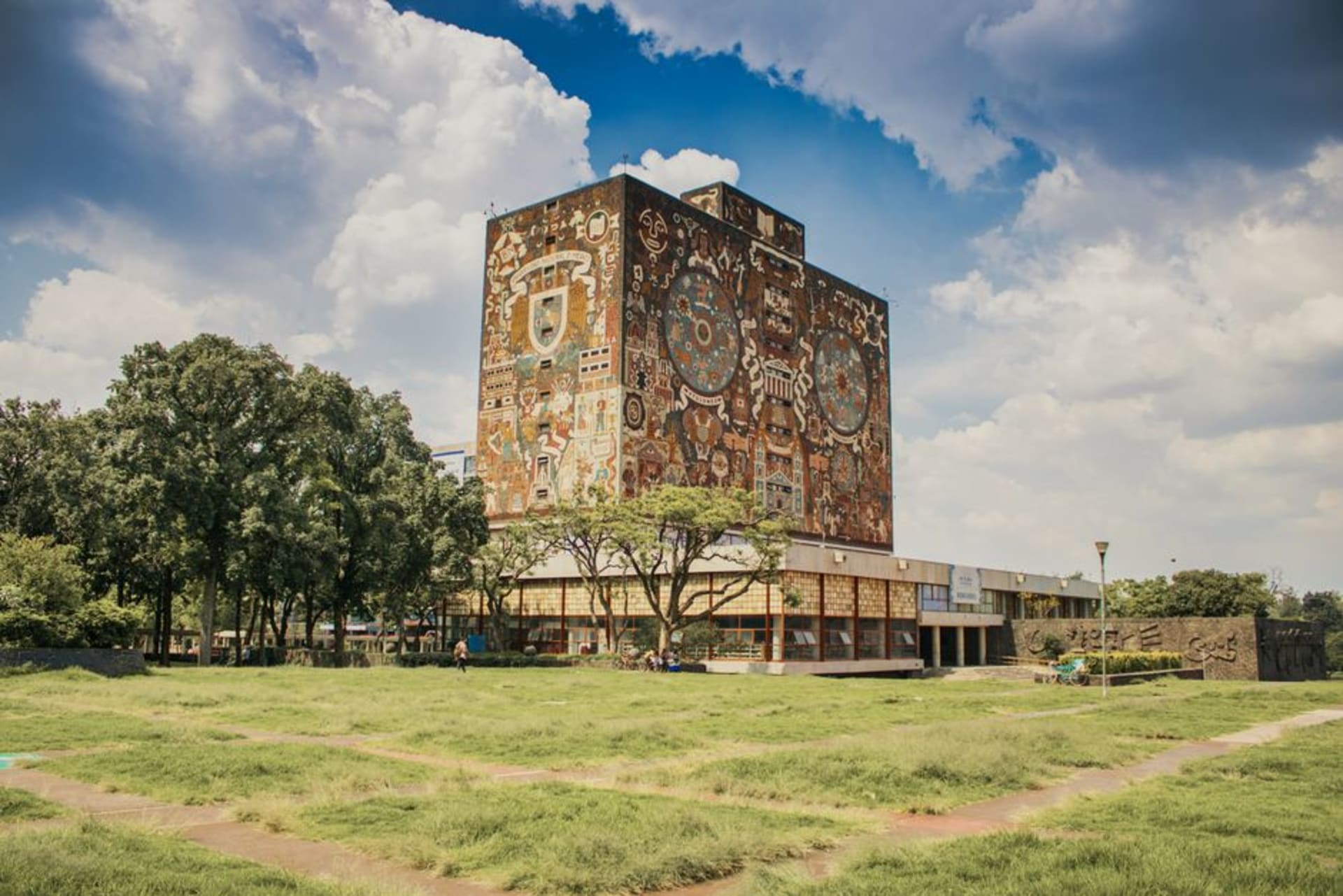 The mosaic-covered facade of the Biblioteca Central at UNAM rising above a volcanic stone esplanade under a wide Mexico City sky
