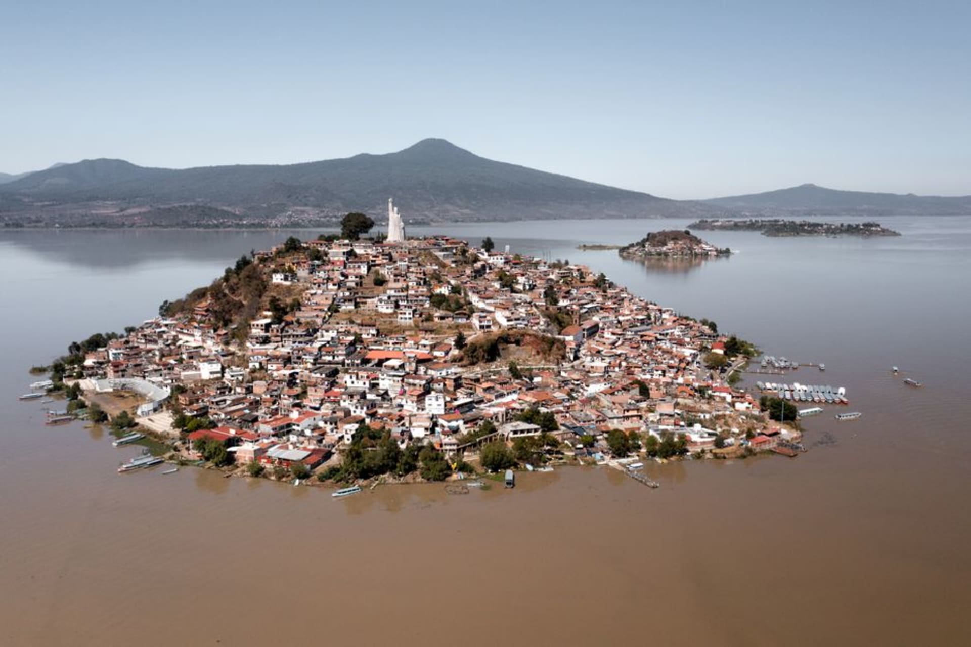 A wooden dock extending into the silver-grey waters of Lake Patzcuaro at dusk, the low hills of the Michoacán shore visible across the water