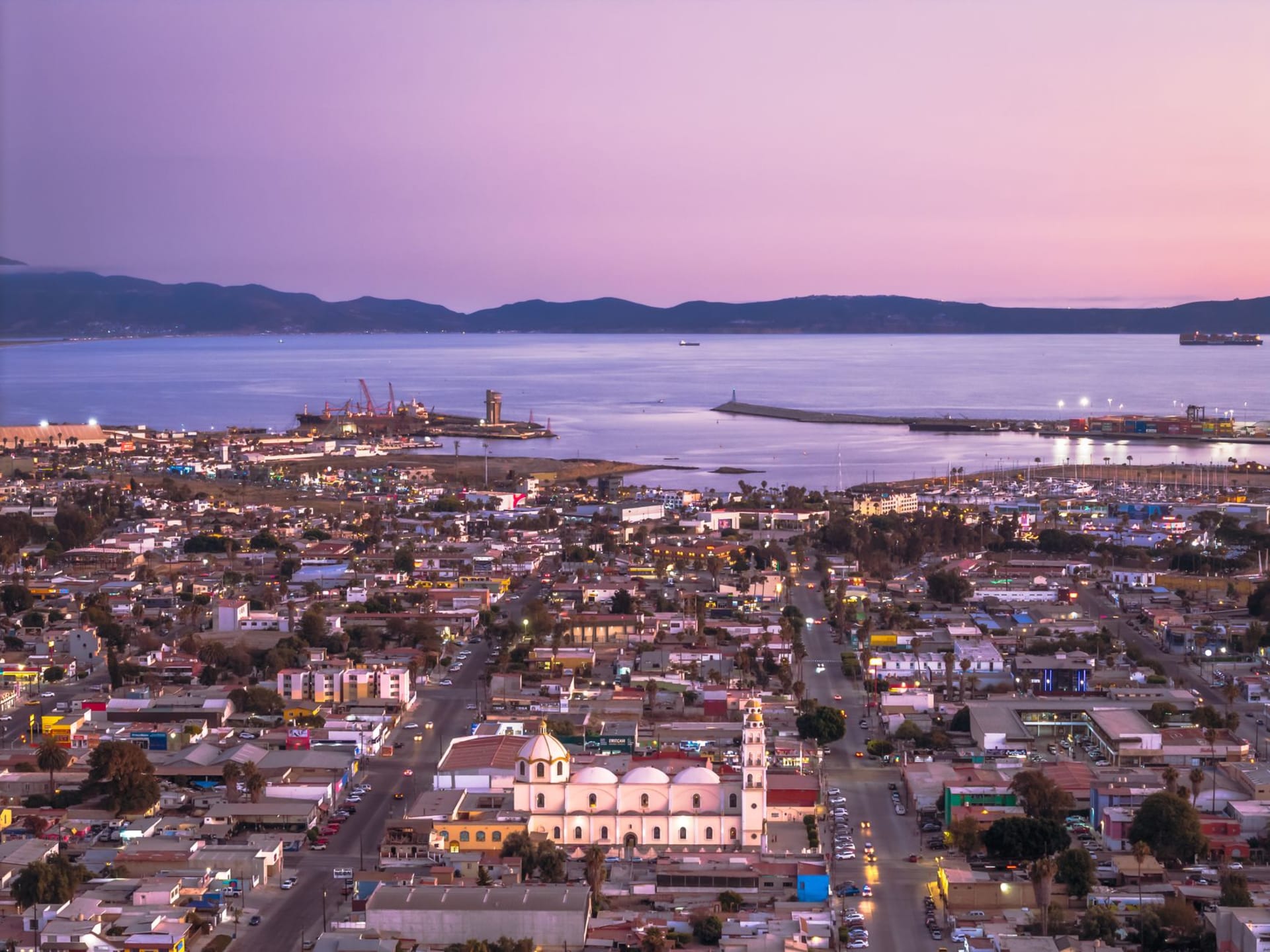 A Hermosillo street at dusk in the Zona Centro, murals on a building facade with orange light, outdoor tables and the energy of a city that doesn't know it's interesting