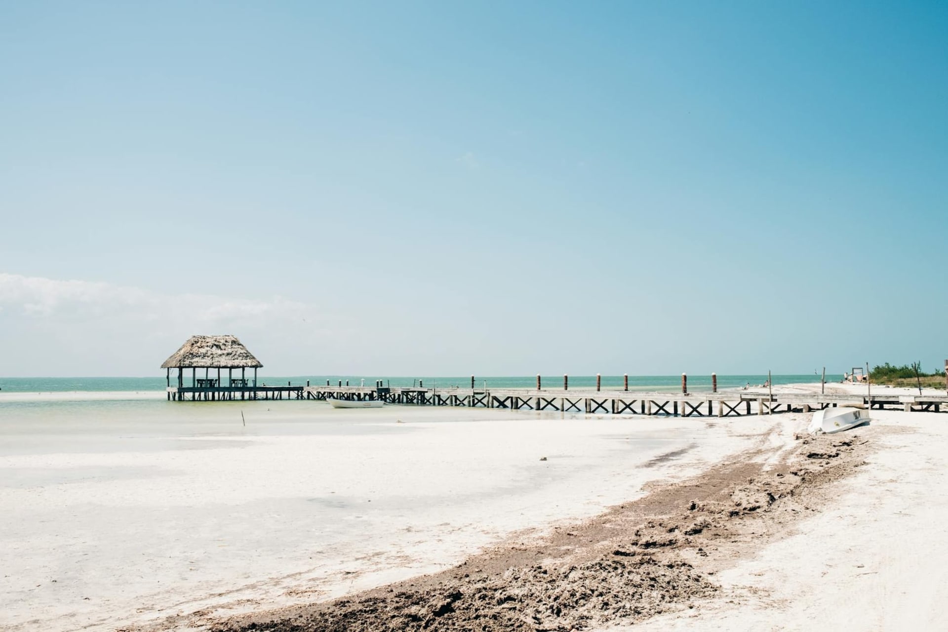 Turquoise shallow water surrounding a wooden hammock dock at Holbox Island, with the Gulf horizon stretching flat and pale under afternoon light