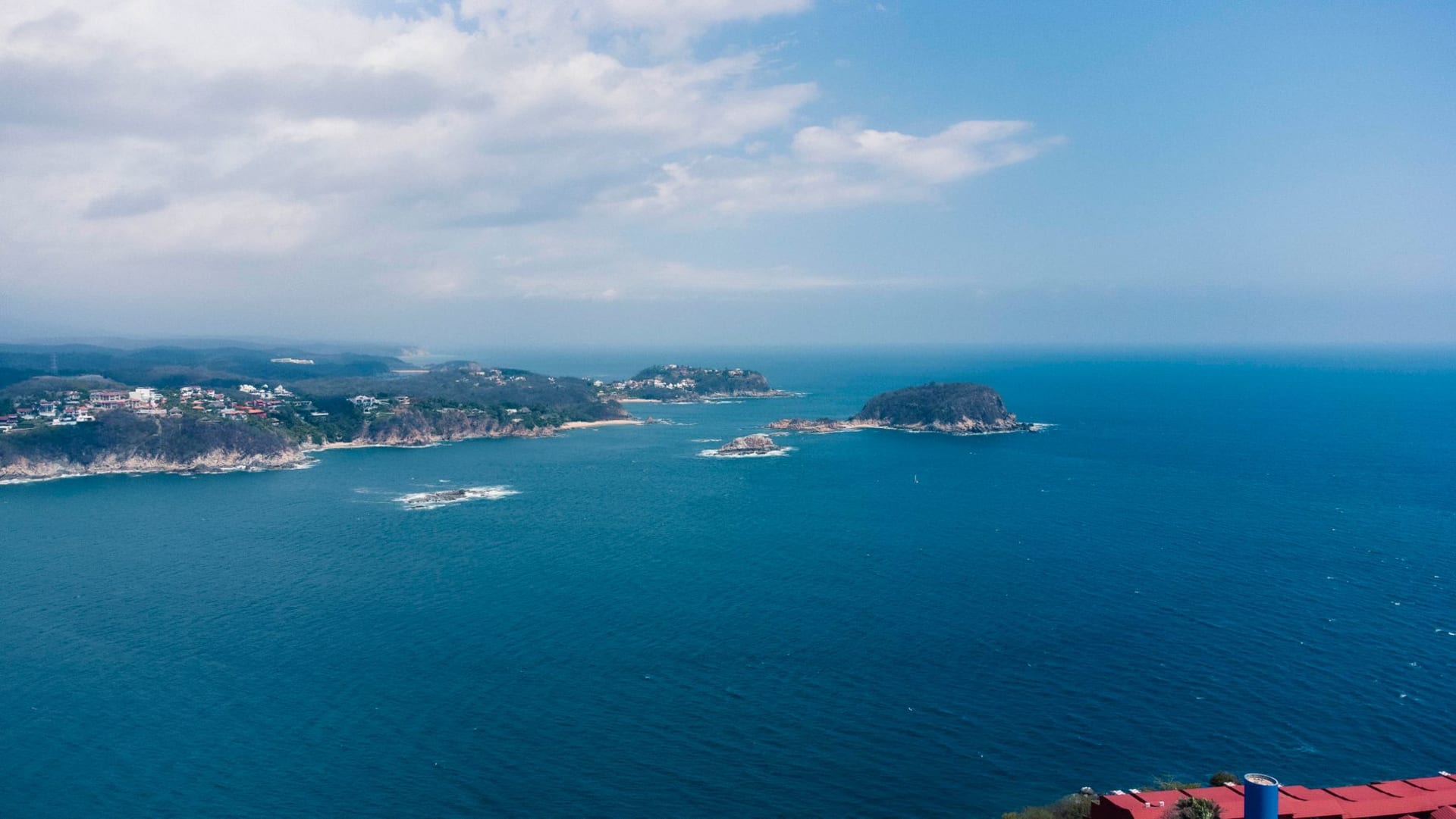 A turquoise Pacific bay in Huatulco enclosed by jungle-covered headlands, a small fishing boat anchored in the calm water with no other development visible