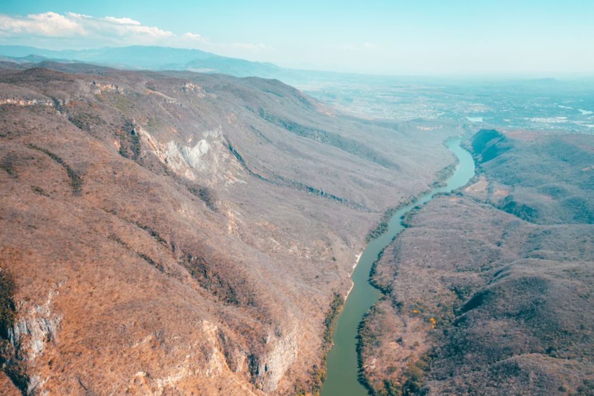 The San Pedro Mezquital river winding through the rust-orange and shadow-green walls of the Barrancas del Nayar, with the village of Huaynamota sitting on a low terrace at the river bend.